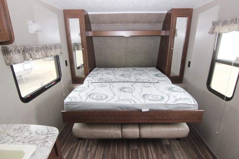 Compact RV rental interior with a space-saving Murphy bed over a sofa, flanked by mirrored cabinets. Ideal for camper living.. Keystone Hideout 2018