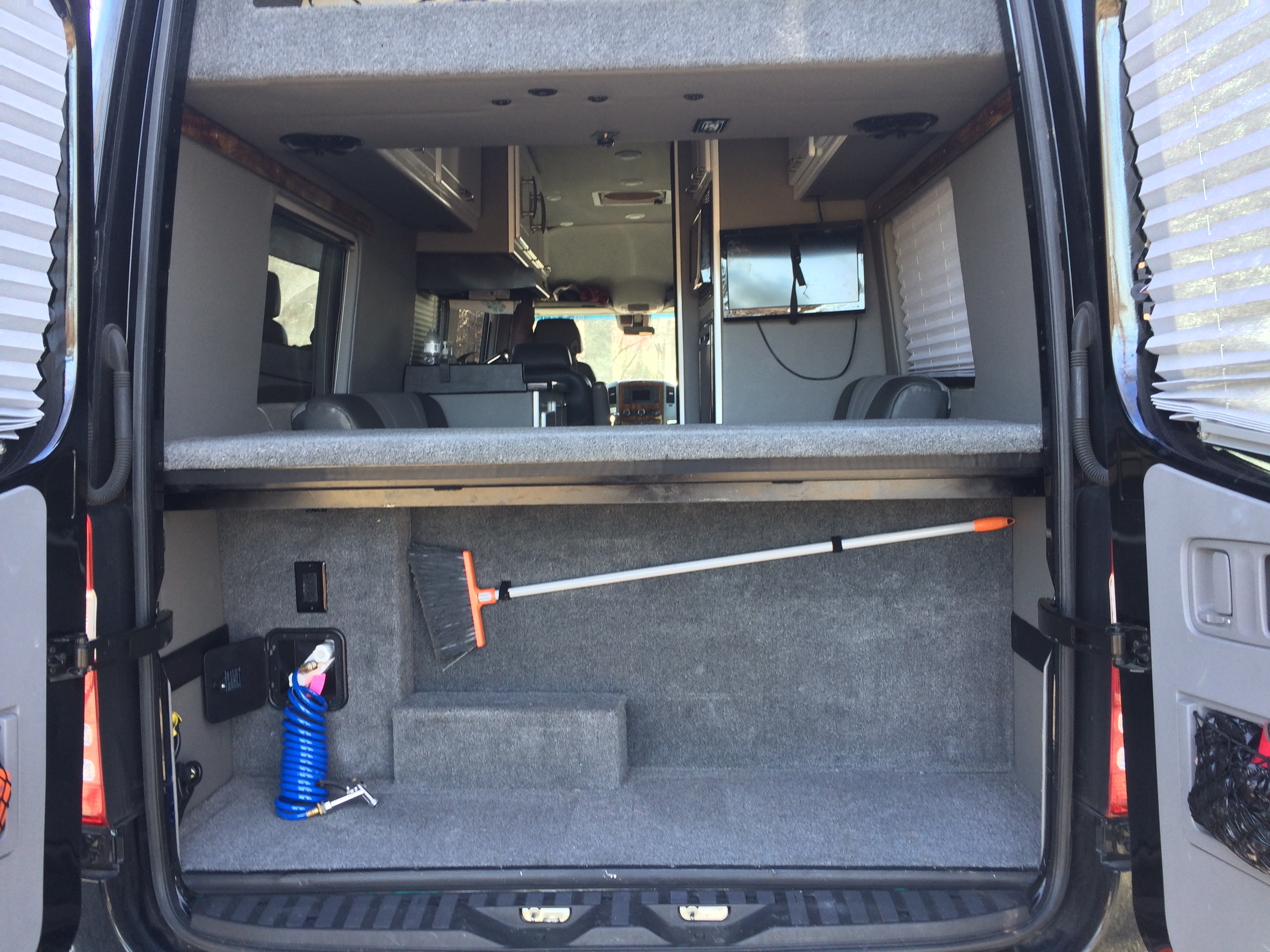 Spacious RV rental interior: two-tier setup with lower carpeted cargo area holding a broom and hose, and an upper bed/storage platform.. Mercedes-Benz 3500 Sprinter 2016