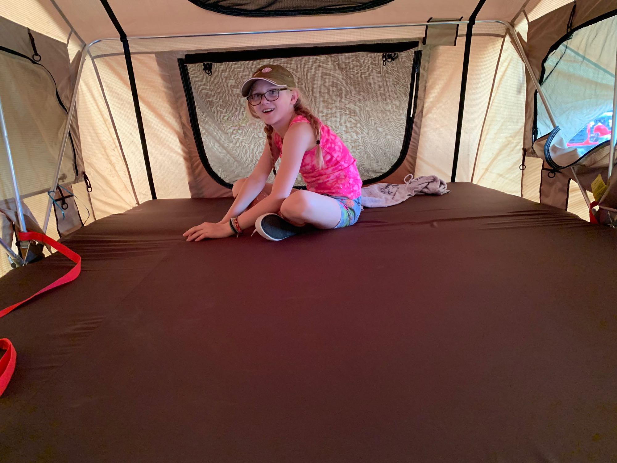 A young girl smiles from inside an RV rental's cozy rooftop tent, ready for camping adventure.. Geared4Utah Smittybilt Scout 2018
