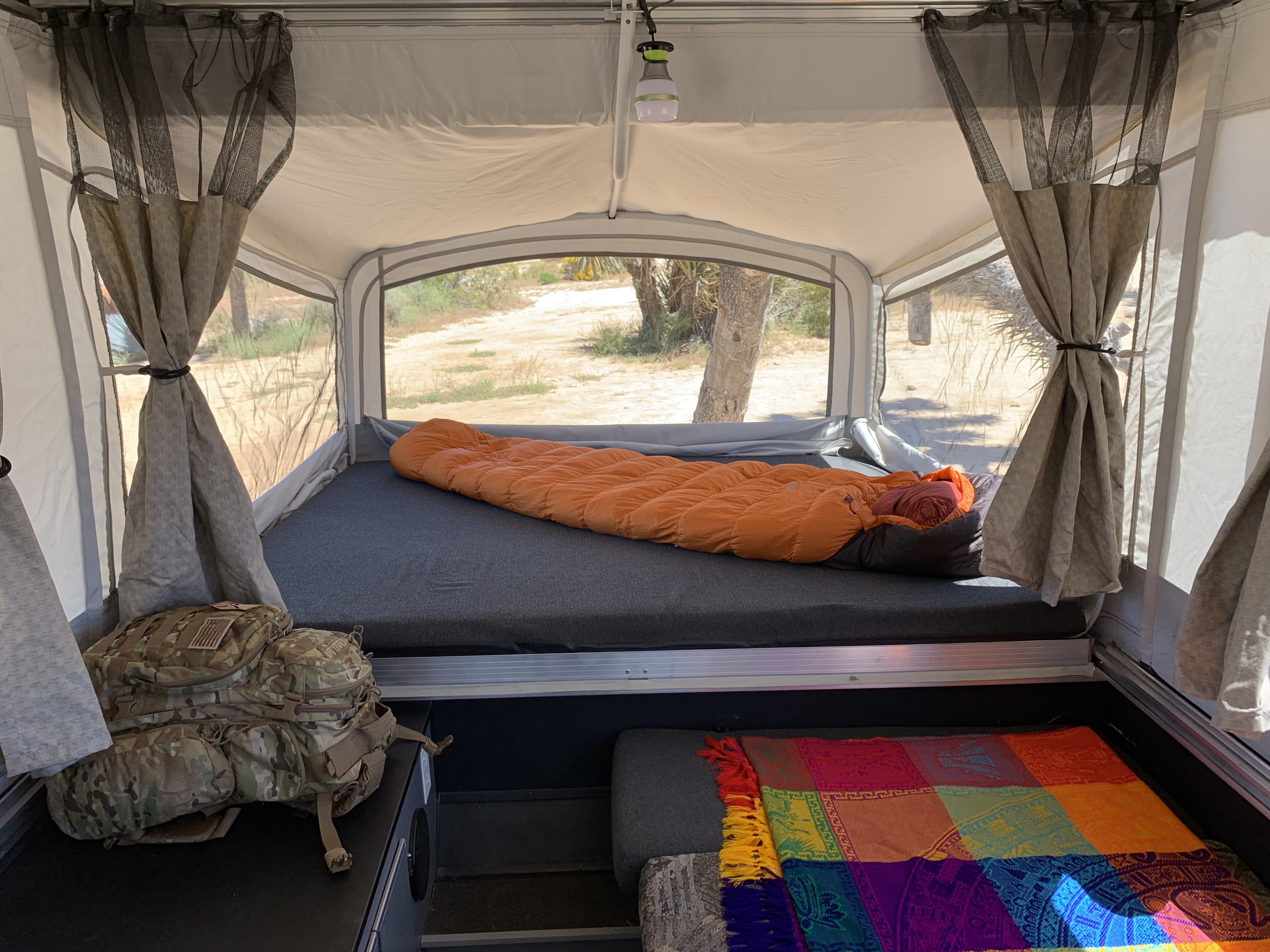 Inside an RV rental pop-up camper: a sleeping bag, colorful blanket, and serene desert views. Great for travel.. Fleetwood Evolution 1 (E1) 2008