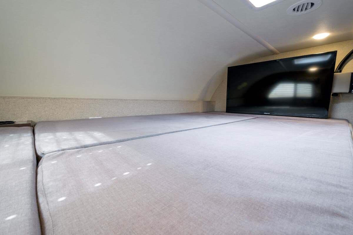 Cozy RV rental cab-over bunk features a comfortable bed and mounted TV, ideal for relaxing after adventures.. Thor Motor Coach Four Winds 2019