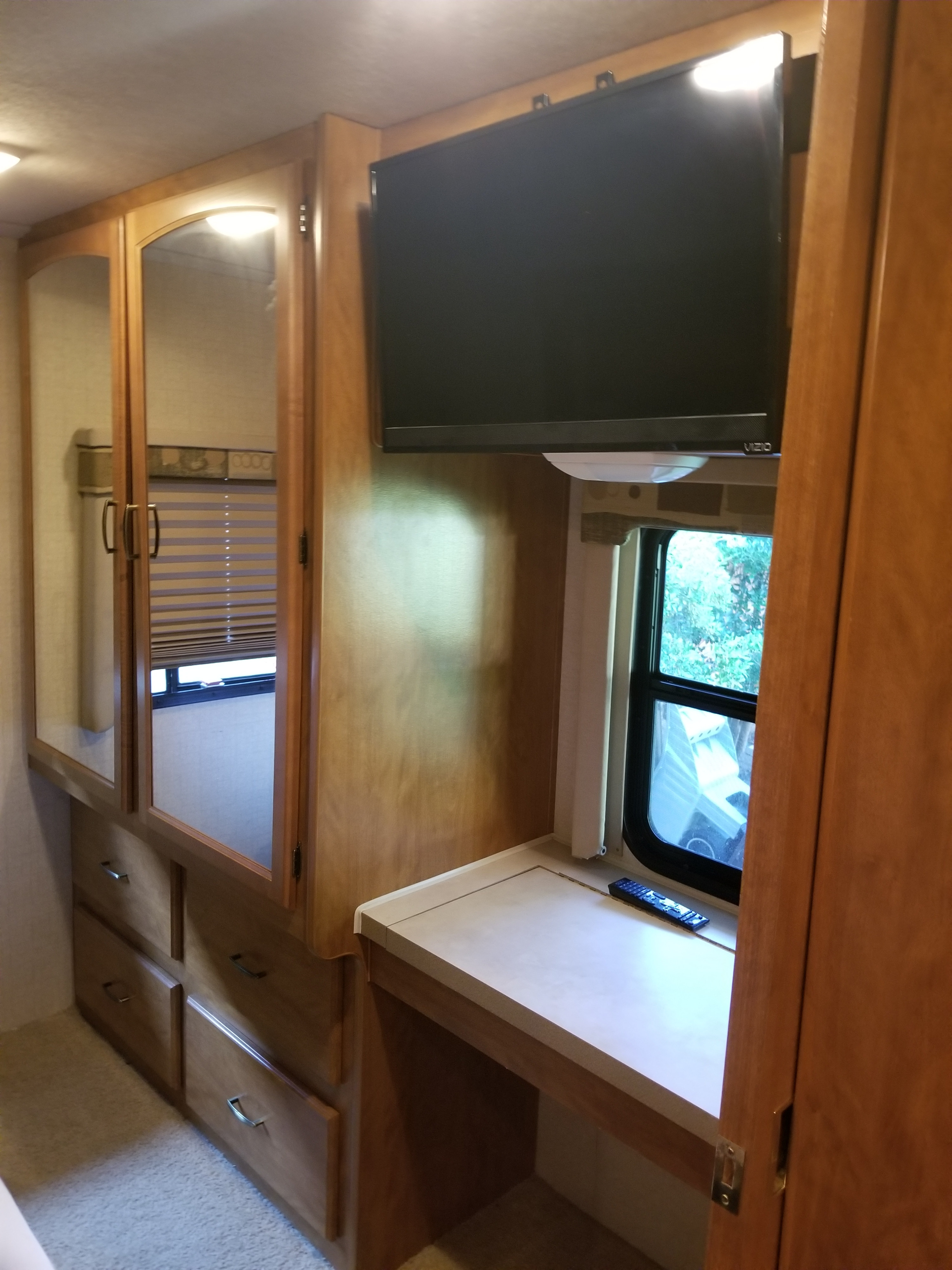 Cozy RV rental interior with built-in wooden cabinetry, a wall-mounted TV, mirrored closet doors, and a small desk by a window.. Tioga Tioga Motorhome 2007