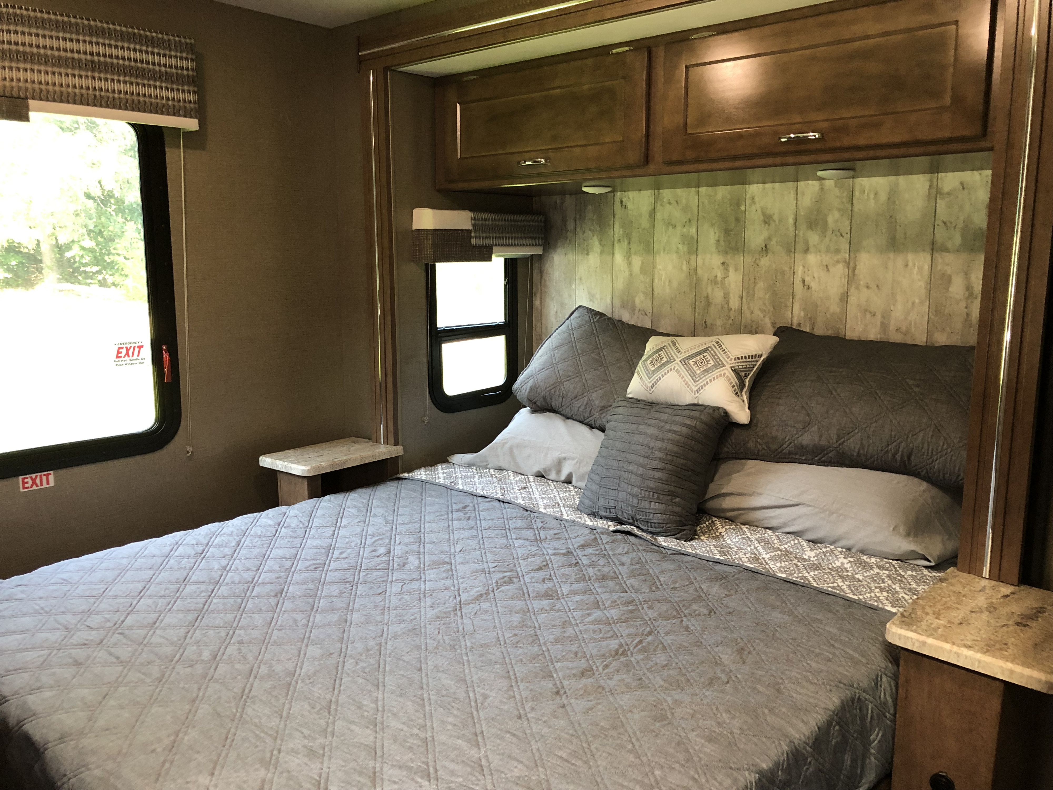 RV rental bedroom interior, showcasing a cozy bed with gray bedding, built-in nightstands, and overhead storage.. Winnebago Outlook 2019