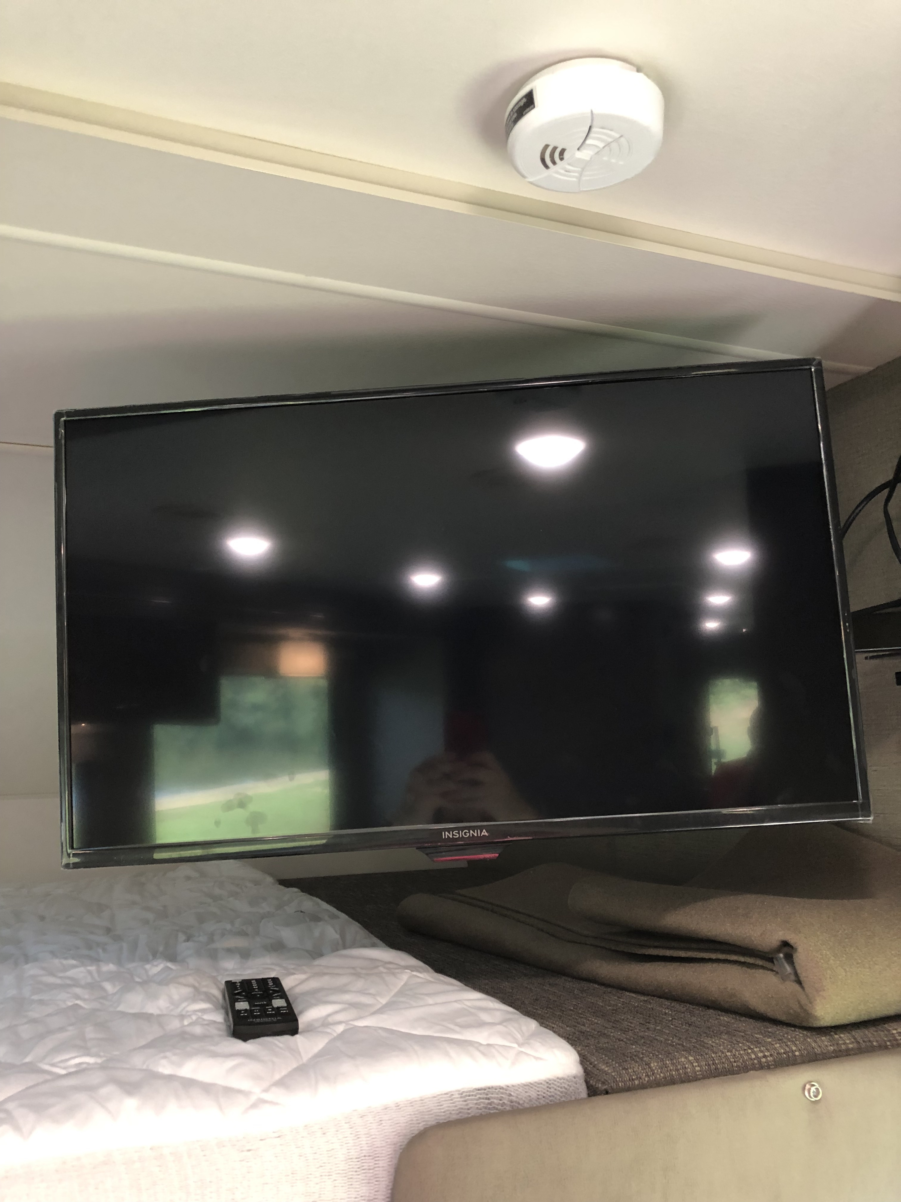 RV rental interior: Insignia TV mounted over bed with remote. Smoke detector visible on ceiling.. Winnebago Outlook 2019