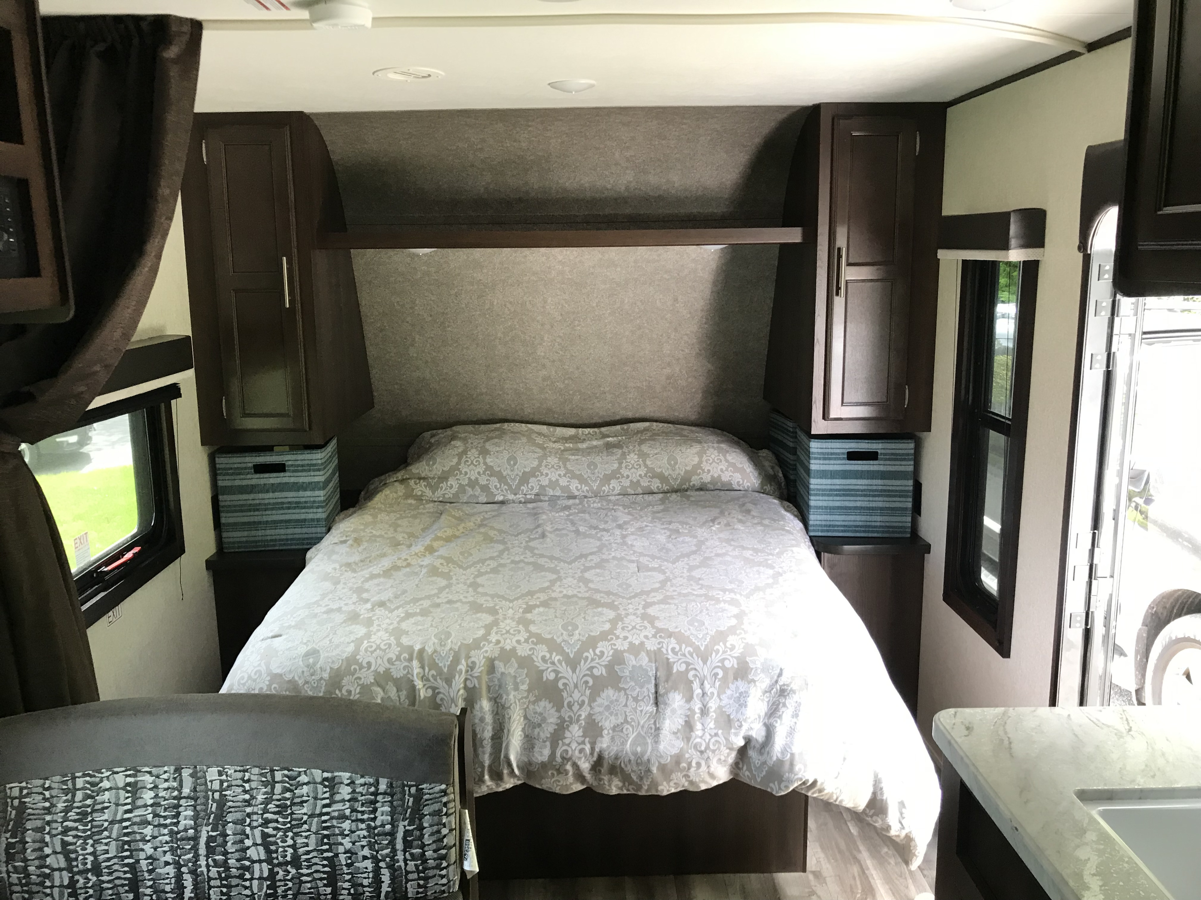 Cozy RV rental bedroom with patterned bedding, wood cabinets, and functional storage bins for a comfortable stay.. Jayco Jay Flight 2019
