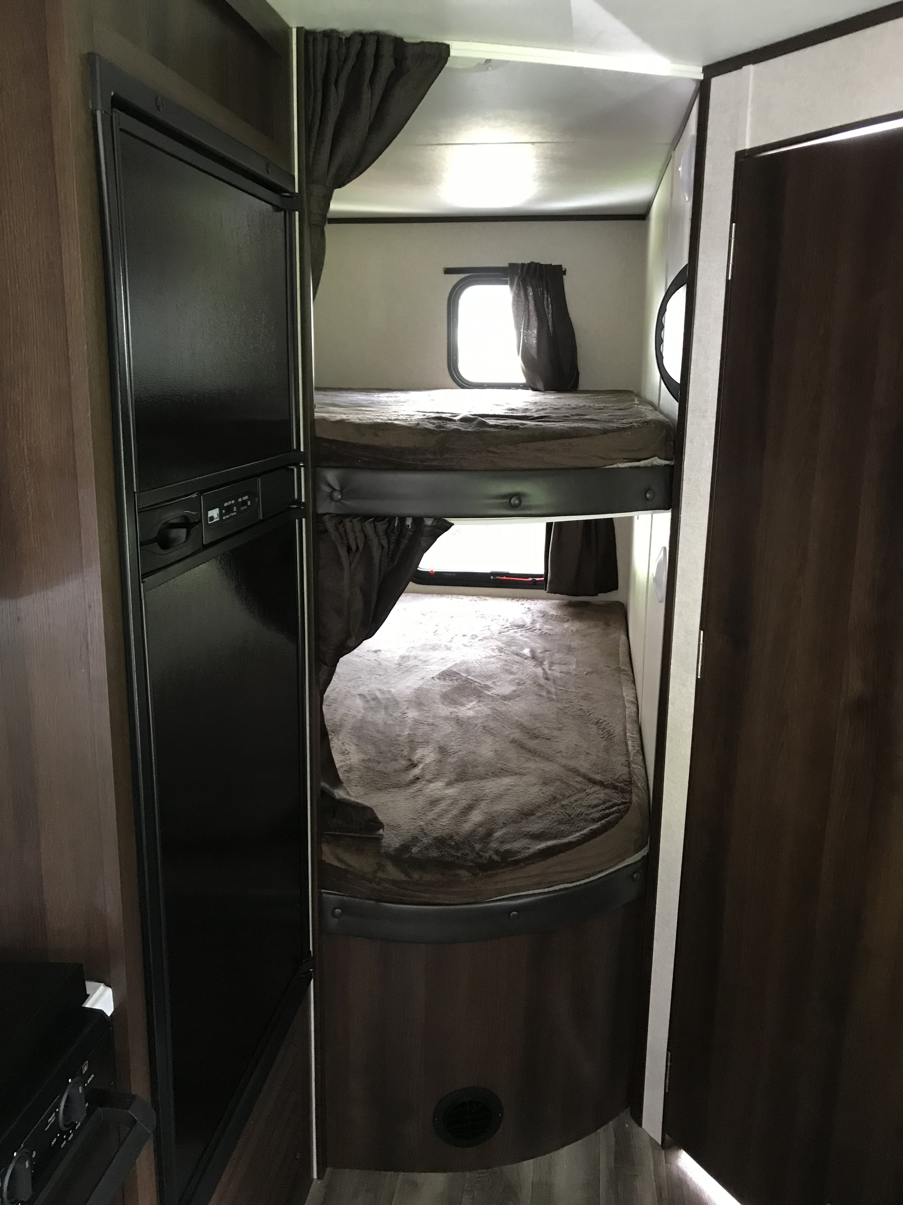 RV rental interior showing a bunk bed sleeping area with two beds, windows, and curtains, adjacent to a built-in refrigerator.. Jayco Jay Flight 2019