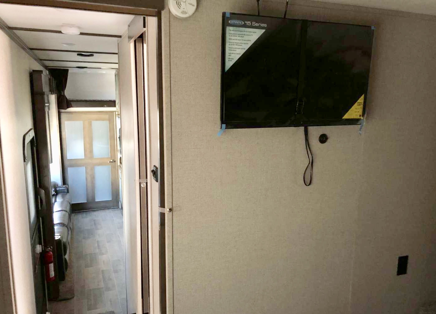 RV rental interior: A flat-screen TV on a textured wall overlooks a narrow hallway with seating and a door.. Dutchmen Voltage 2019