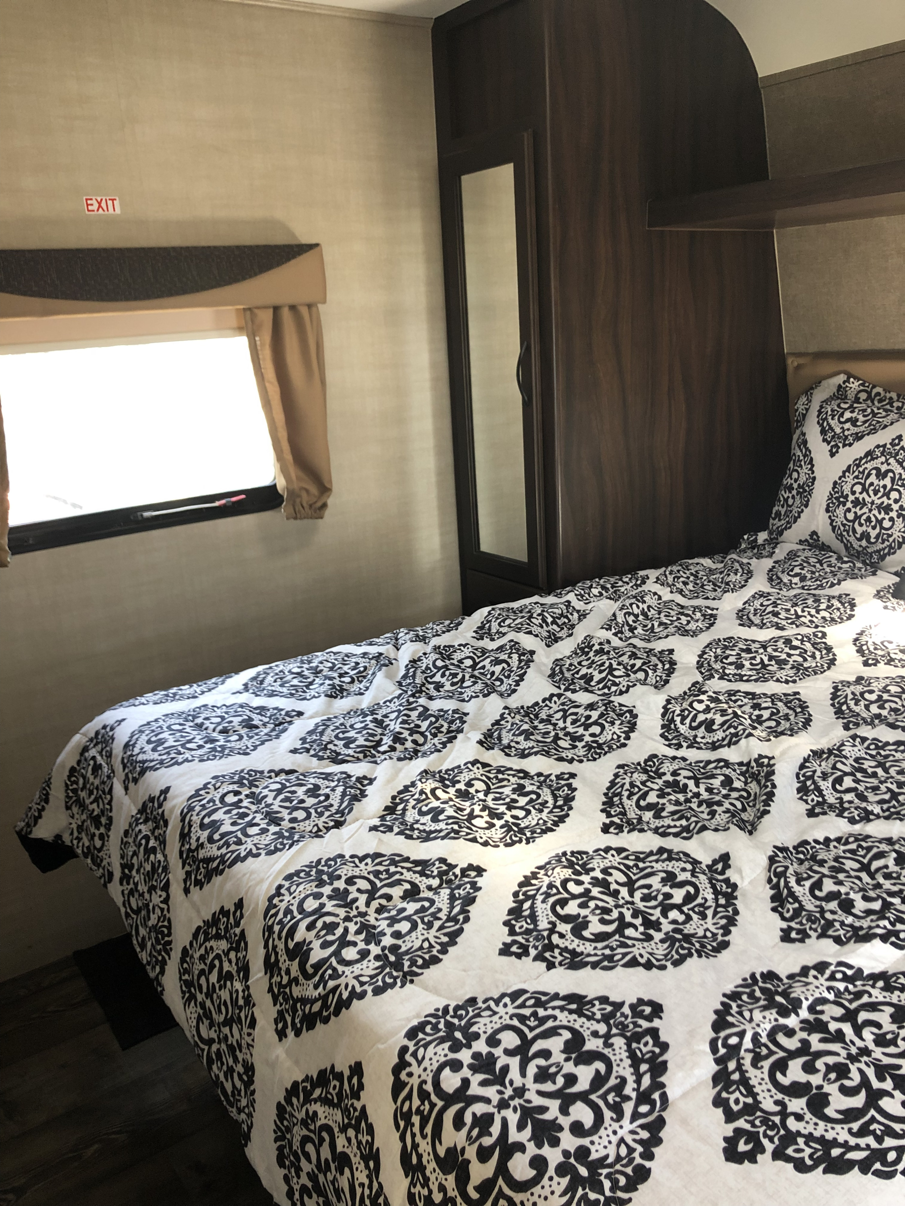 Inside an RV rental bedroom with a white and black patterned comforter, exit window, and wood cabinetry.. Pacific Coachworks Panther BHSS 2019