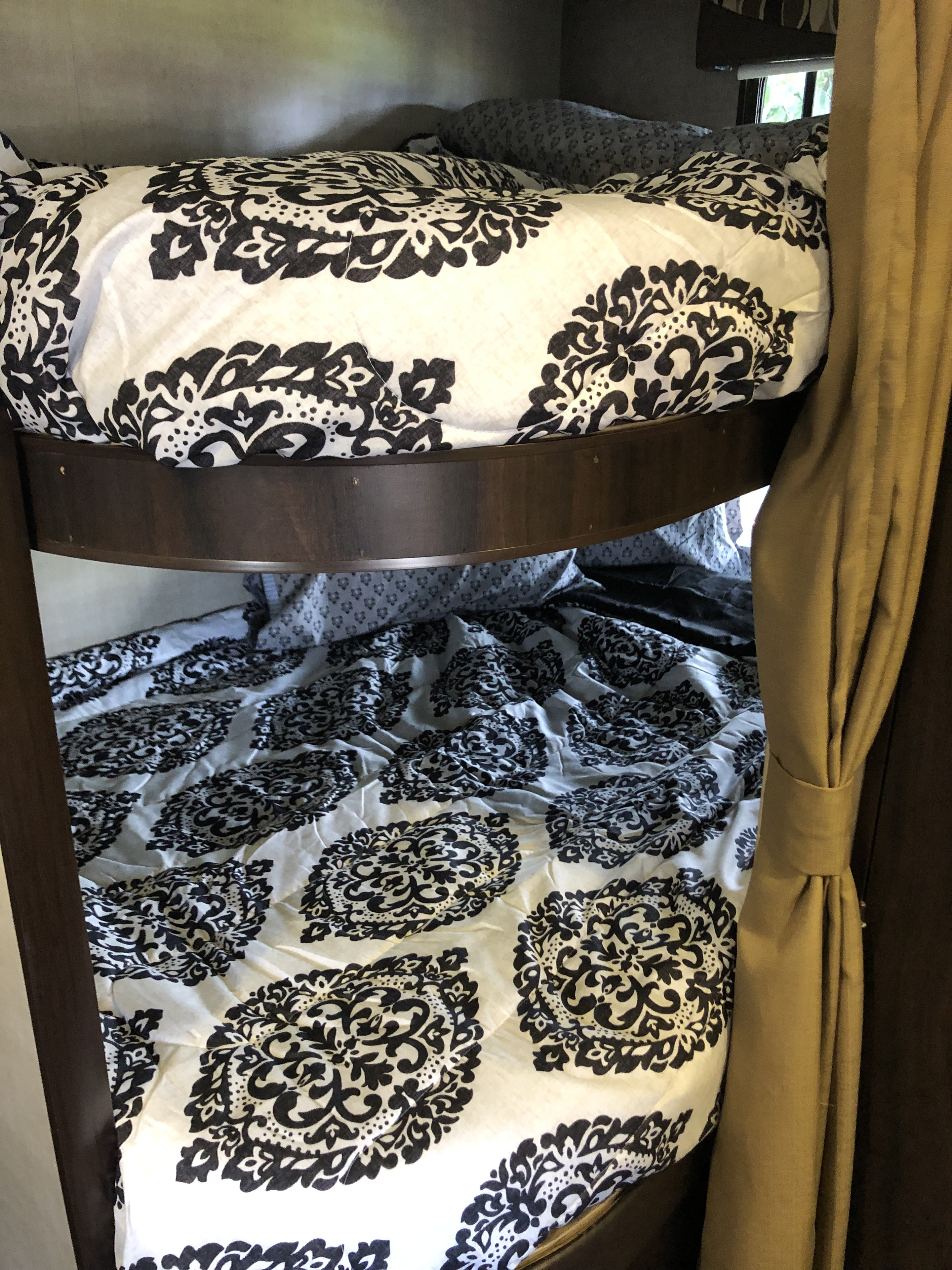 Inside an **RV rental**, cozy bunk beds with black and white patterned bedding, dark wood frame, and a light brown curtain.. Pacific Coachworks Panther BHSS 2019