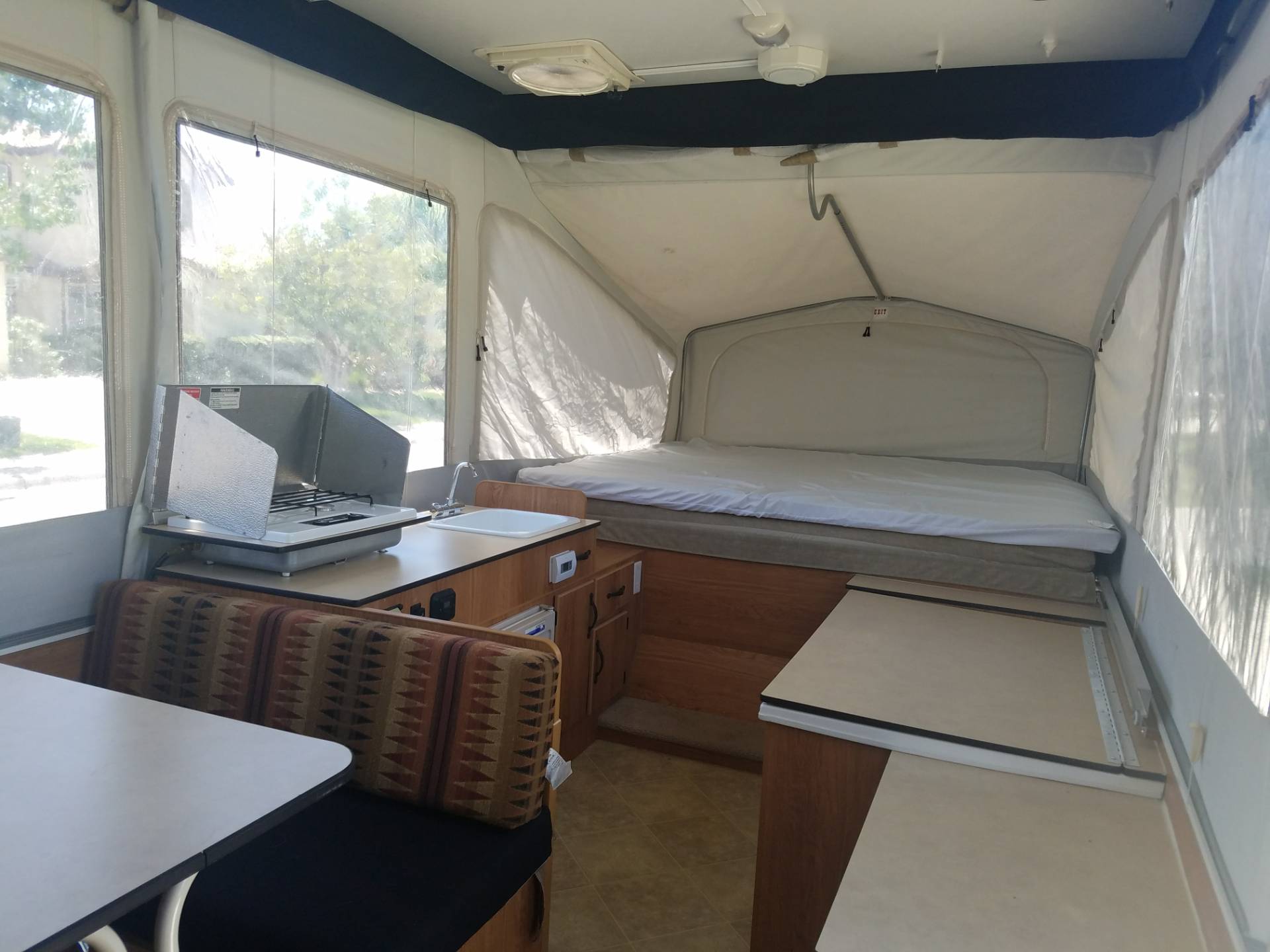Spacious pop-up RV rental interior with kitchen, dining area, and bed. Enjoy comfortable camping.. Jayco Baja 2006