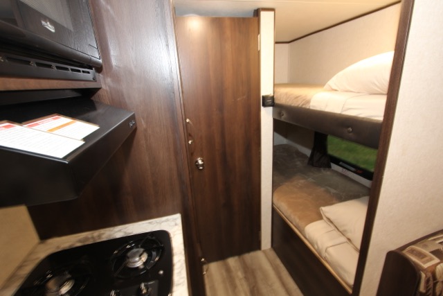 Inside an RV rental: a compact kitchen with microwave, a door, and stacked bunk beds.. Jayco Jay Flight 2018