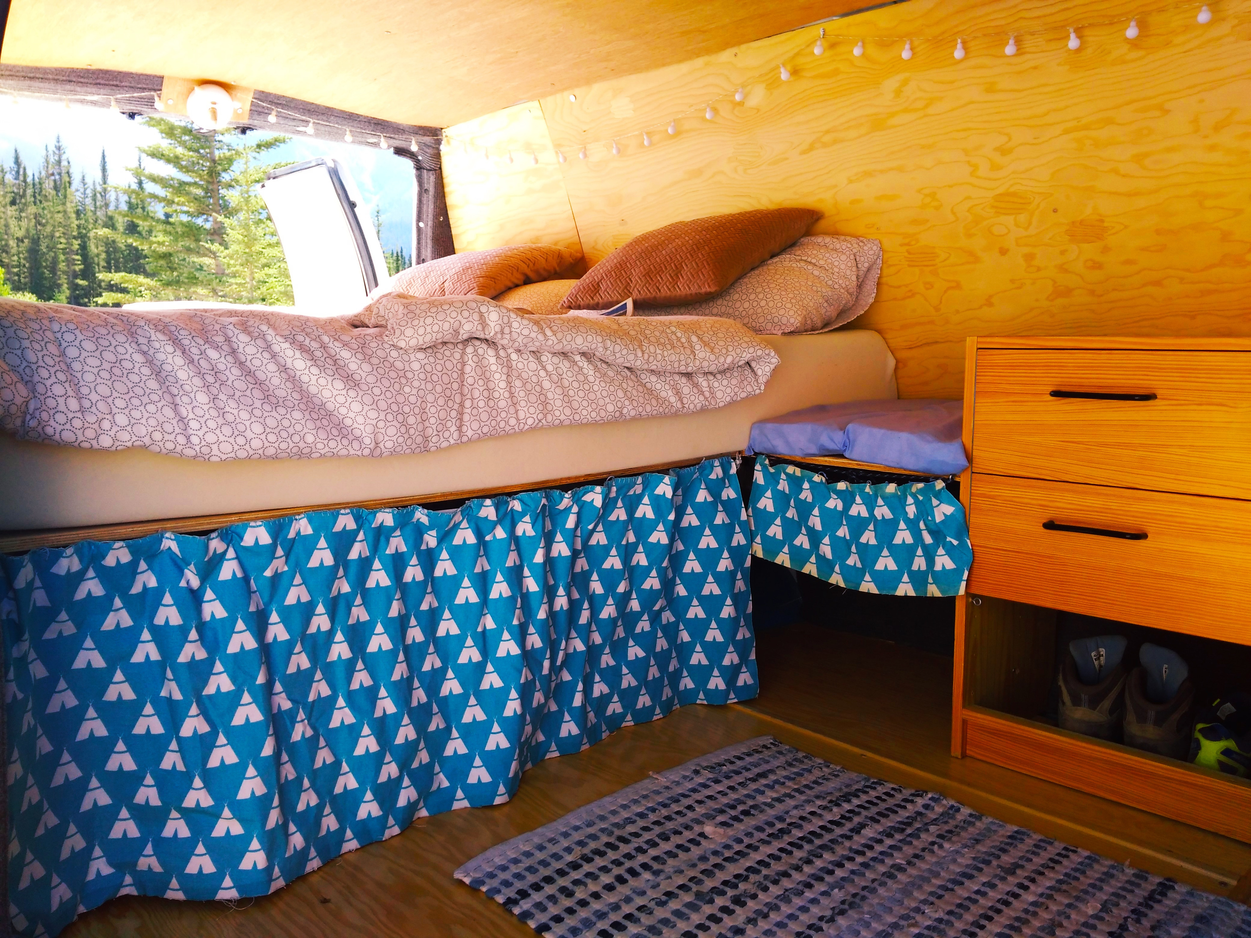 Cozy RV rental interior with a comfy bed, wooden walls, unique teepee-patterned storage curtains, and forest views.. Ford Econoline 2006