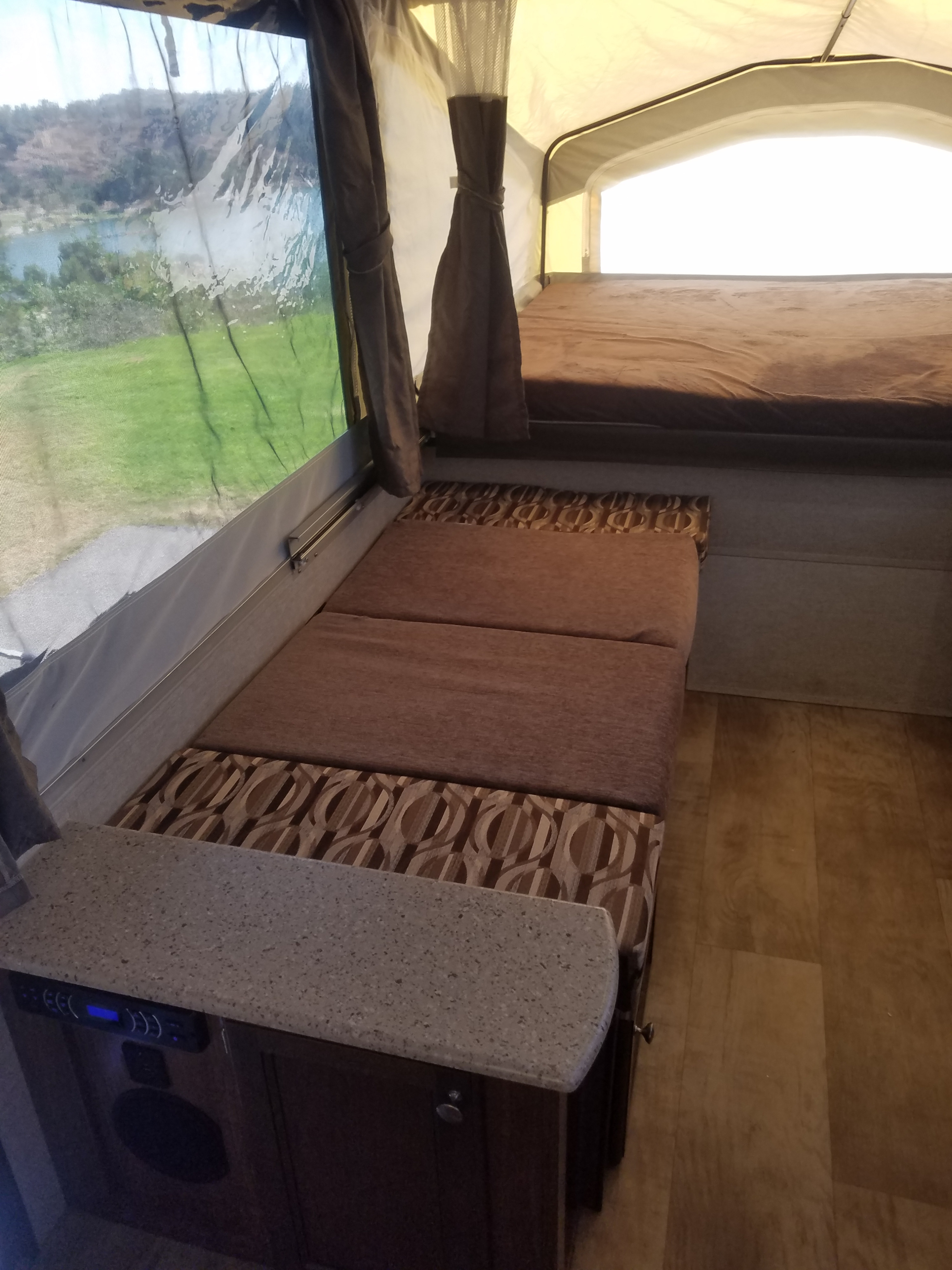 Interior of a pop-up camper for RV rental: shows bed, seating, counter, & scenic lake view outside.. Palomino Real Lite Real-Lite 2017