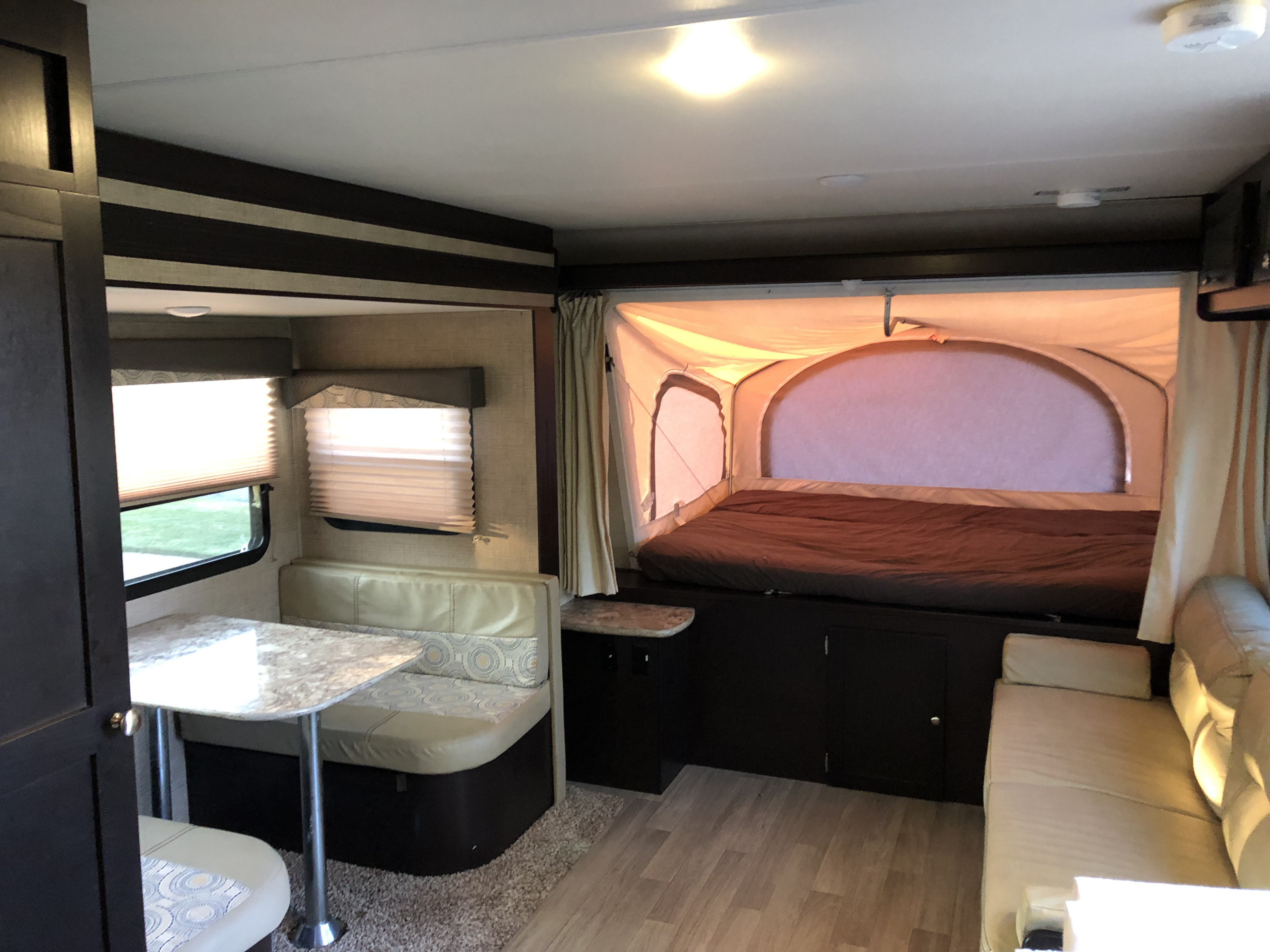 Bright RV rental interior featuring a large pop-out bed, a dinette with table, and a sofa. Ideal for comfortable travel.. Dutchmen Kodiak 2016
