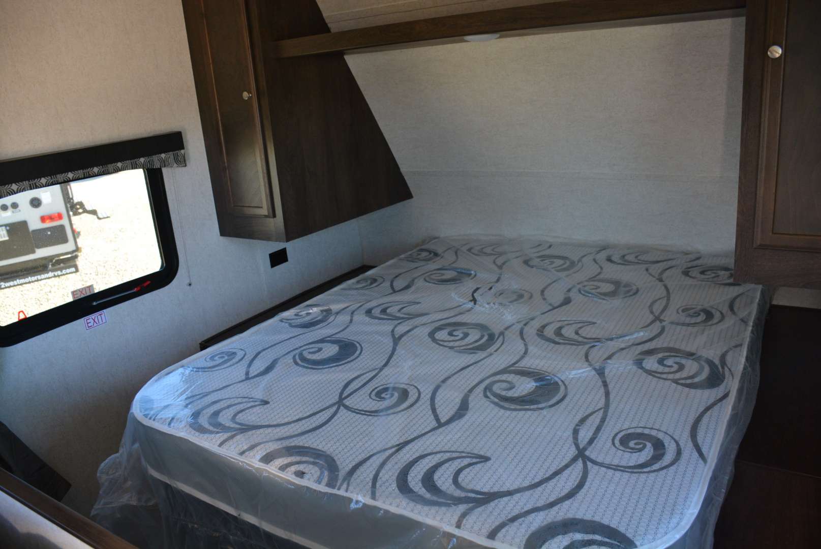 Inside an RV rental bedroom with a plastic-wrapped mattress, overhead storage, and an emergency exit window.. Starcraft Autumn Ridge 2019