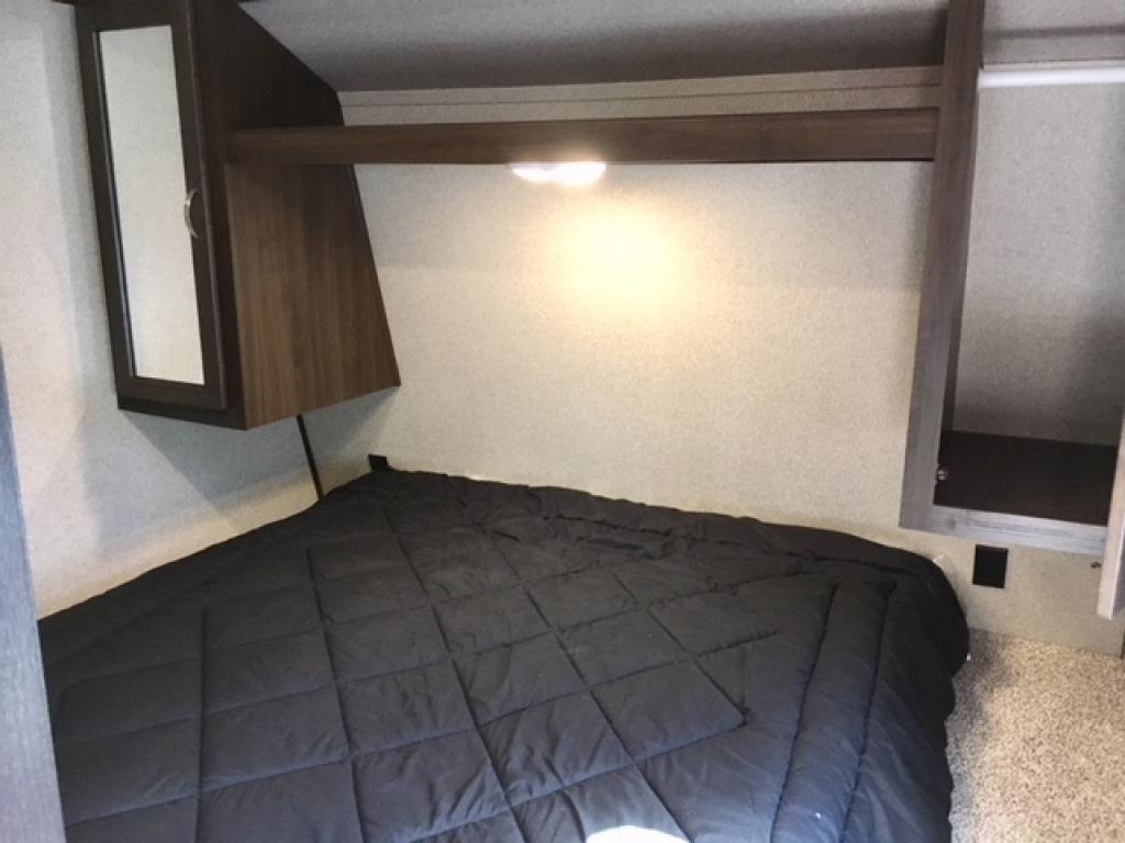 Cozy RV rental bedroom with a comfy black bed, overhead storage, and mirror. Ideal for travel comfort.. springdale limited 2019