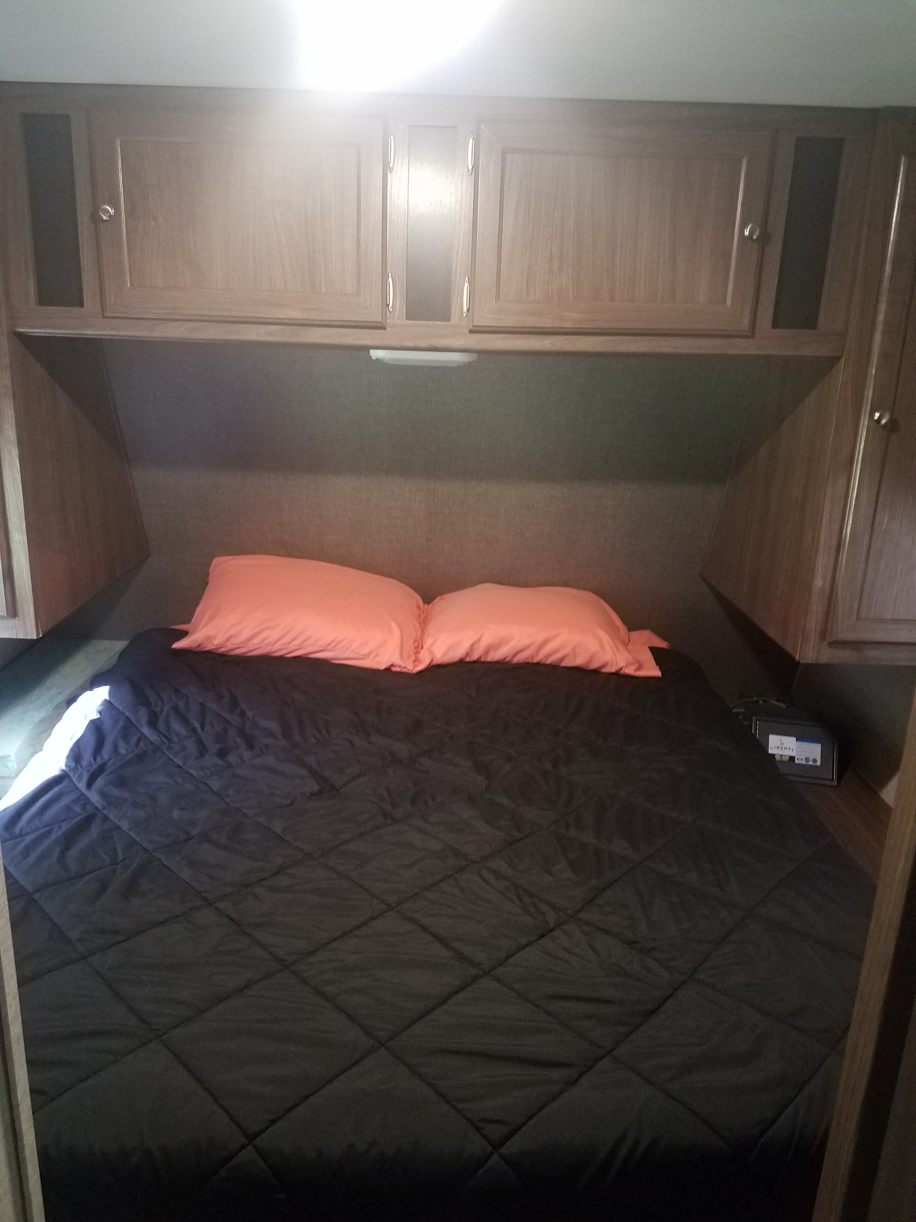 Compact RV rental bedroom featuring a comfy bed with orange pillows and built-in overhead cabinets, ideal for road trips.. Heartland Pioneer 2016