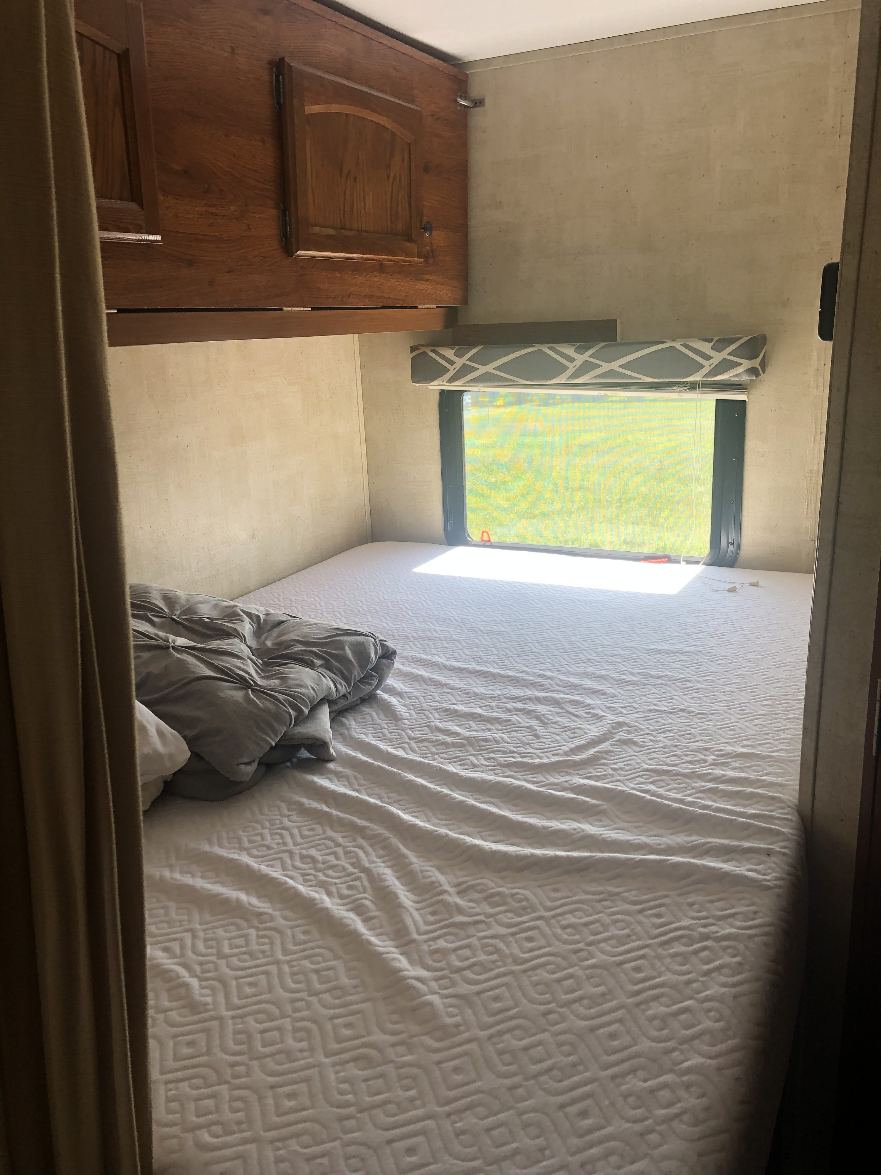 RV rental bedroom with bed, cabinets, and window. Sunlight brightens the compact sleeping area.. Keystone Hideout 2016