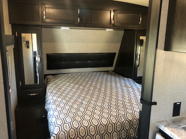 Experience a compact RV rental bedroom with a patterned bed, black headboard, and dark wood cabinets, ideal for travelers.. Grand Design Other 2020