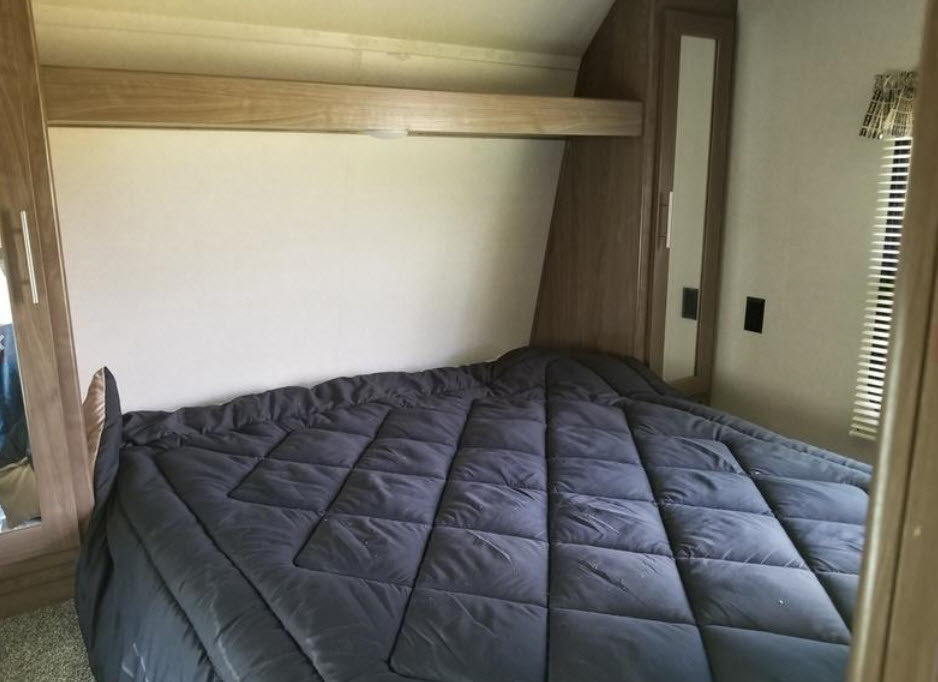 Cozy RV rental bedroom featuring a dark quilted comforter, built-in cabinetry, and a window for comfortable travel.. Keystone Hideout 2017
