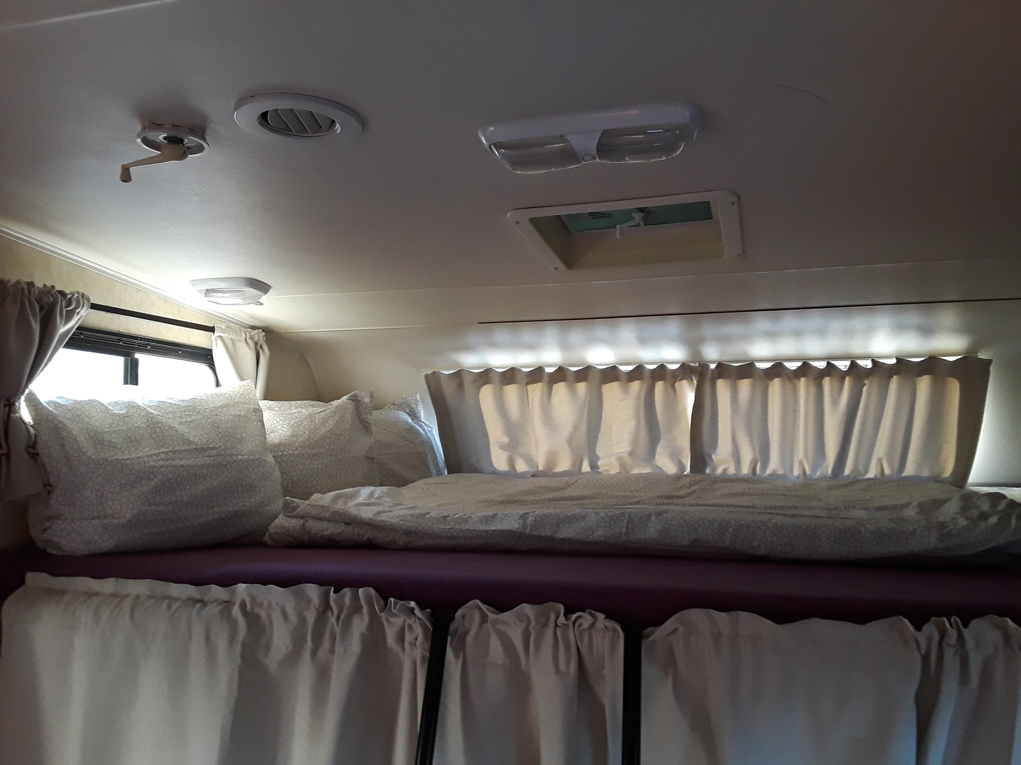 Cozy RV rental interior showcasing a comfortable bed, curtains, ceiling lights, and vents.. Coachmen Freelander 2011