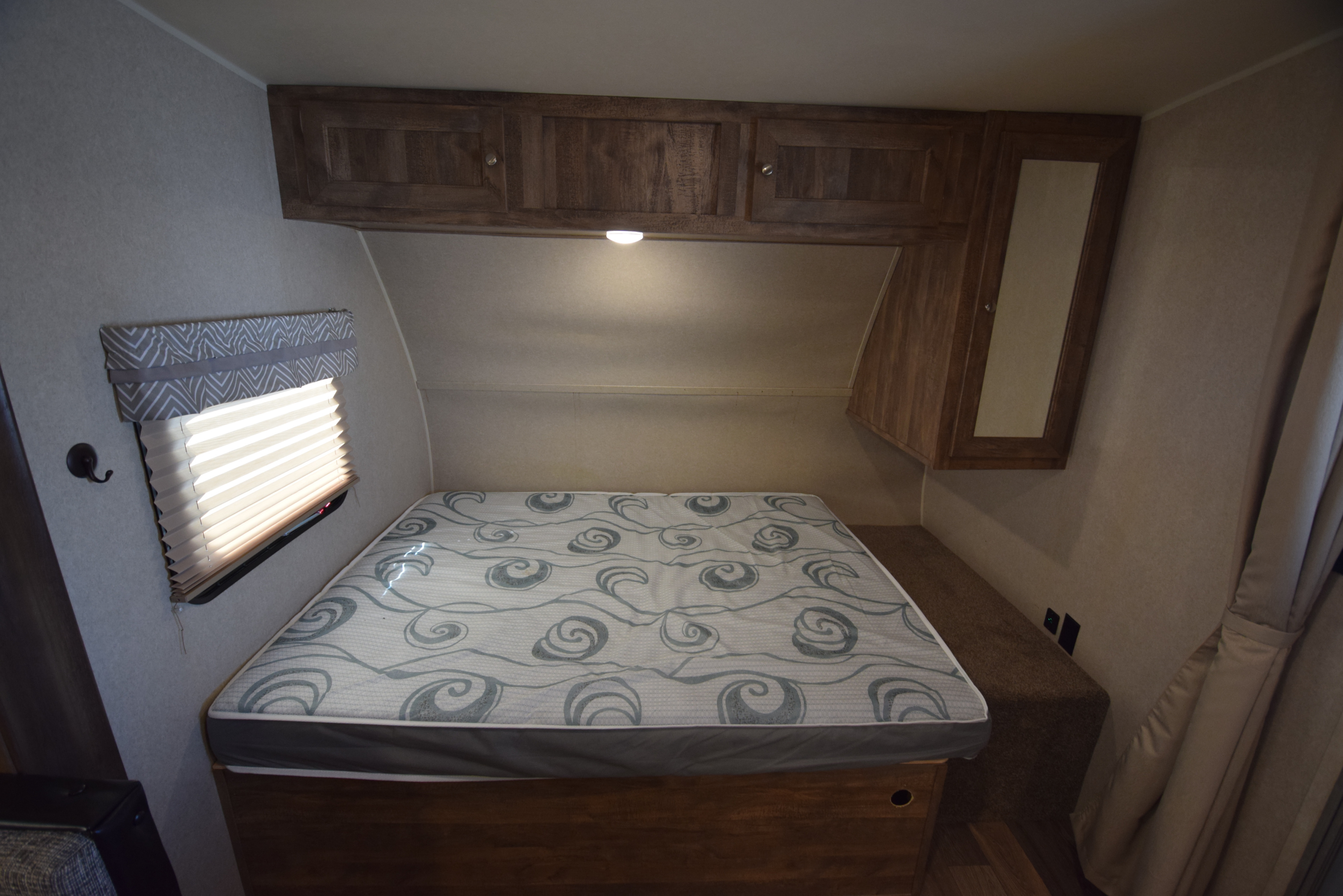 Cozy RV rental bedroom showing a bed with a patterned mattress, overhead wood cabinets, and a window with blinds.. Palomino Puma XLE 2019