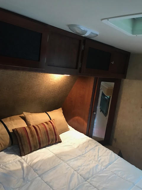 Cozy RV rental bedroom showing a bed with white comforter, pillows, dark wood cabinets, and warm lighting.. Dutchmen Kodiak 2013