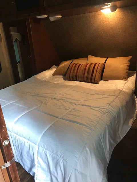 Cozy RV rental bedroom featuring a large bed with white comforter, pillows, and warm overhead lighting. Perfect for travel.. Dutchmen Kodiak 2013