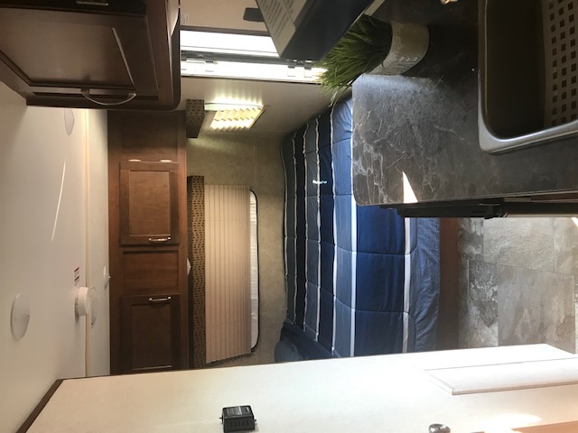 This RV rental interior features a cozy bedroom with blue striped bedding, a well-equipped kitchen counter, and wood storage cabinets.. Jayco Jay Flight SLX 2017
