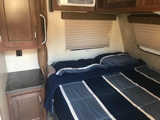 Comfortable RV rental bedroom featuring a striped bed, cabinets, and windows with blinds. Ideal for road trips.. Jayco Jay Flight SLX 2017