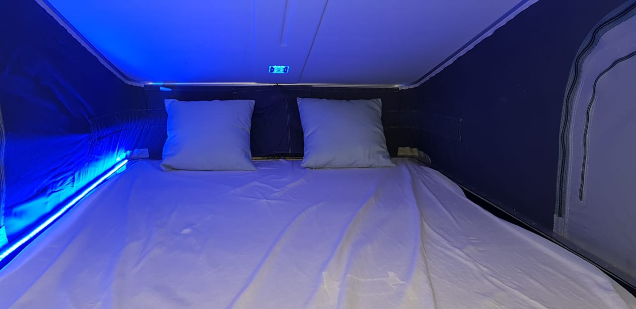 An inviting RV rental sleeping area featuring a bed with two pillows and ambient blue LED strip lighting.. Renault Trafic 2019