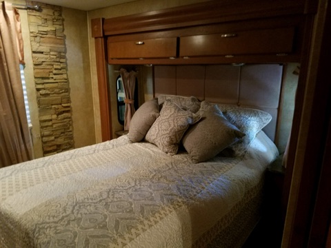 Comfortable RV rental bedroom featuring a patterned bed, stone wall, and built-in storage.. Forest River Other 2011