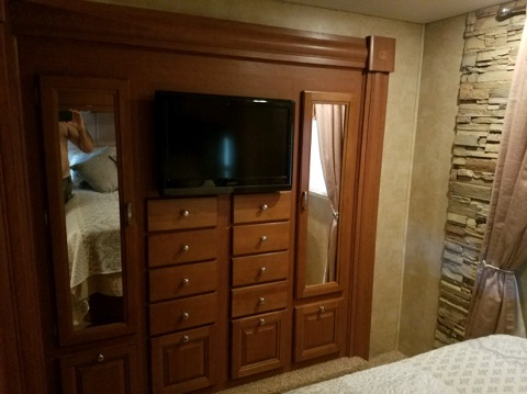 RV rental bedroom: wood storage unit with TV & mirrored doors, cozy bed, and stone accent wall.. Forest River Other 2011