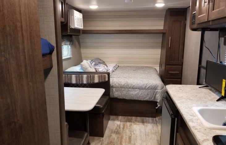 RV rental interior showcasing a cozy bedroom area, dinette seating, and compact kitchen with sink and TV.. Crossroads RV Zinger Lite 2019