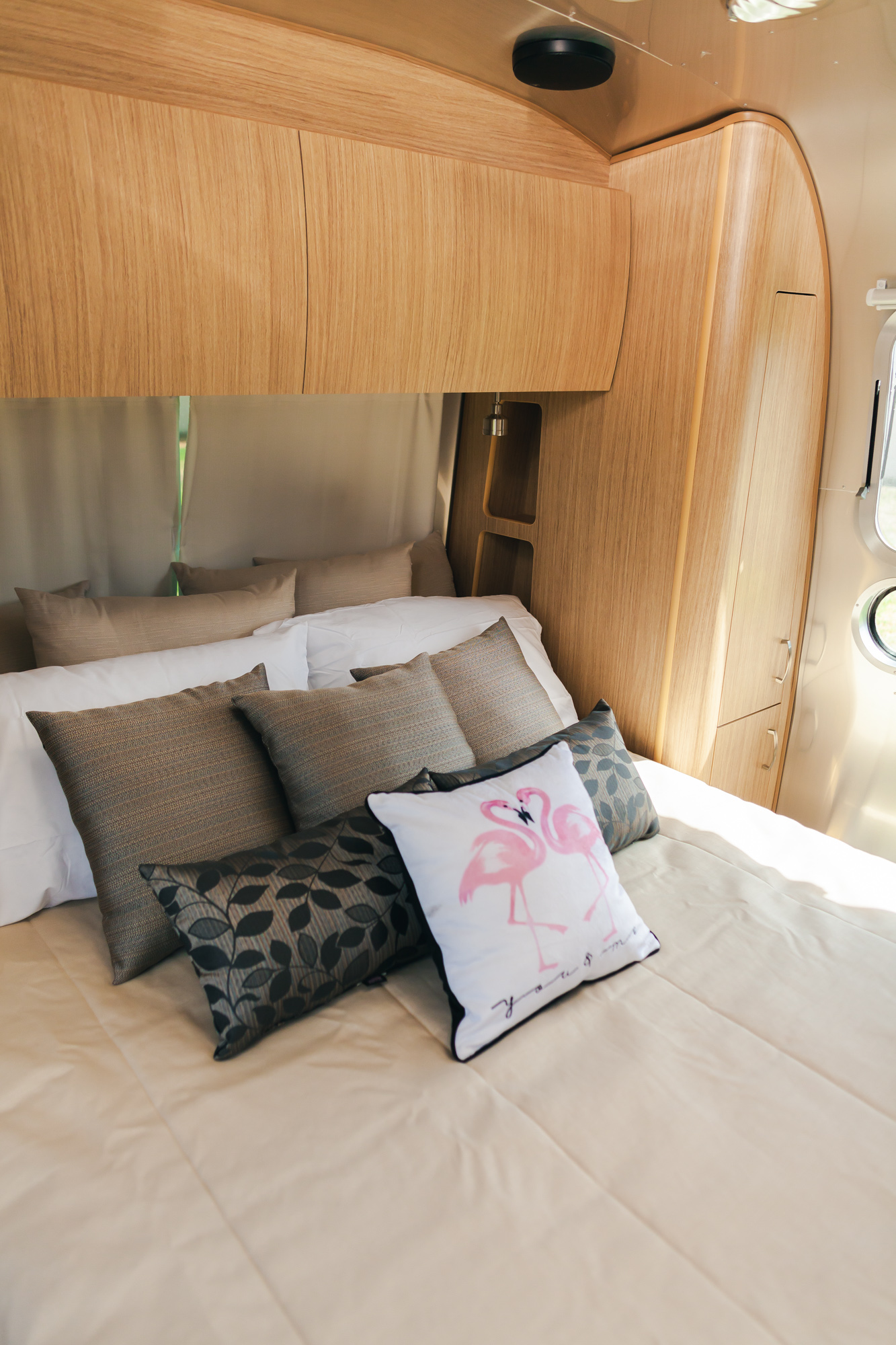 Cozy RV rental bedroom featuring a comfortable bed, light wood interior, and a fun flamingo pillow. Relax and travel.. Airstream Flying Cloud 2020