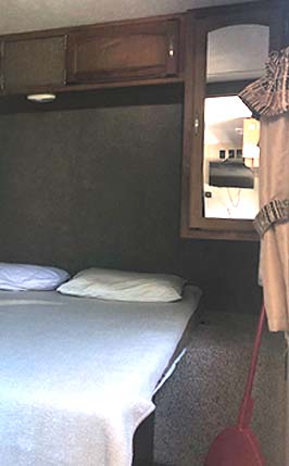 Compact RV rental bedroom interior with a bed, overhead cabinets, and mirrored storage, ideal for travel.. Keystone Springdale 2017