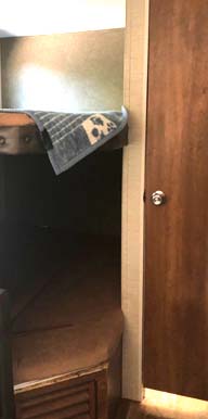 Compact RV rental interior showing a bunk bed with a patterned towel, a lower mattress, and a wooden door.. Keystone Springdale 2017