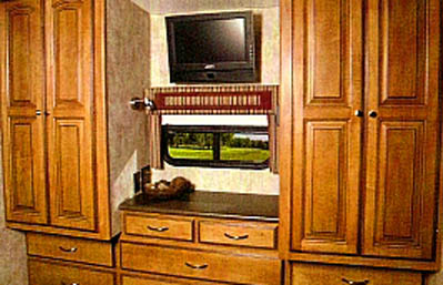 RV rental interior: warm wood cabinetry, TV, and window showcasing a green field view.. Winnebago Vista 2011