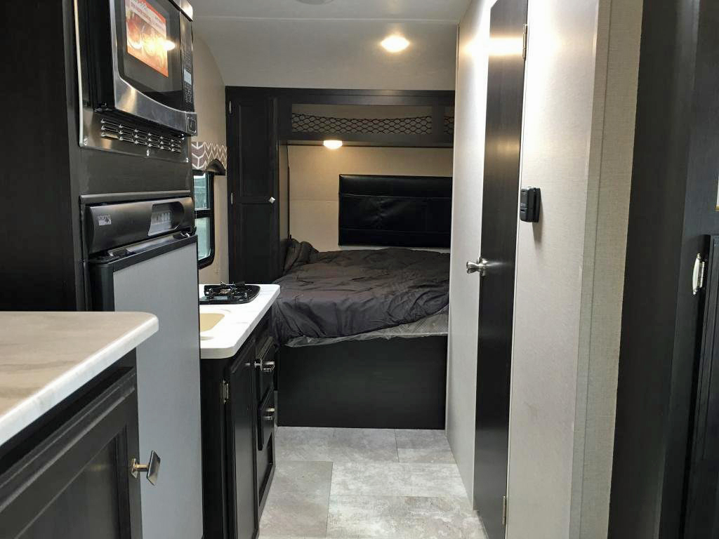 Compact RV rental interior featuring a full kitchen with microwave, fridge, and stovetop, plus a comfortable bedroom area.. Venture Rv Sonic Lite SL 169VRD 2018