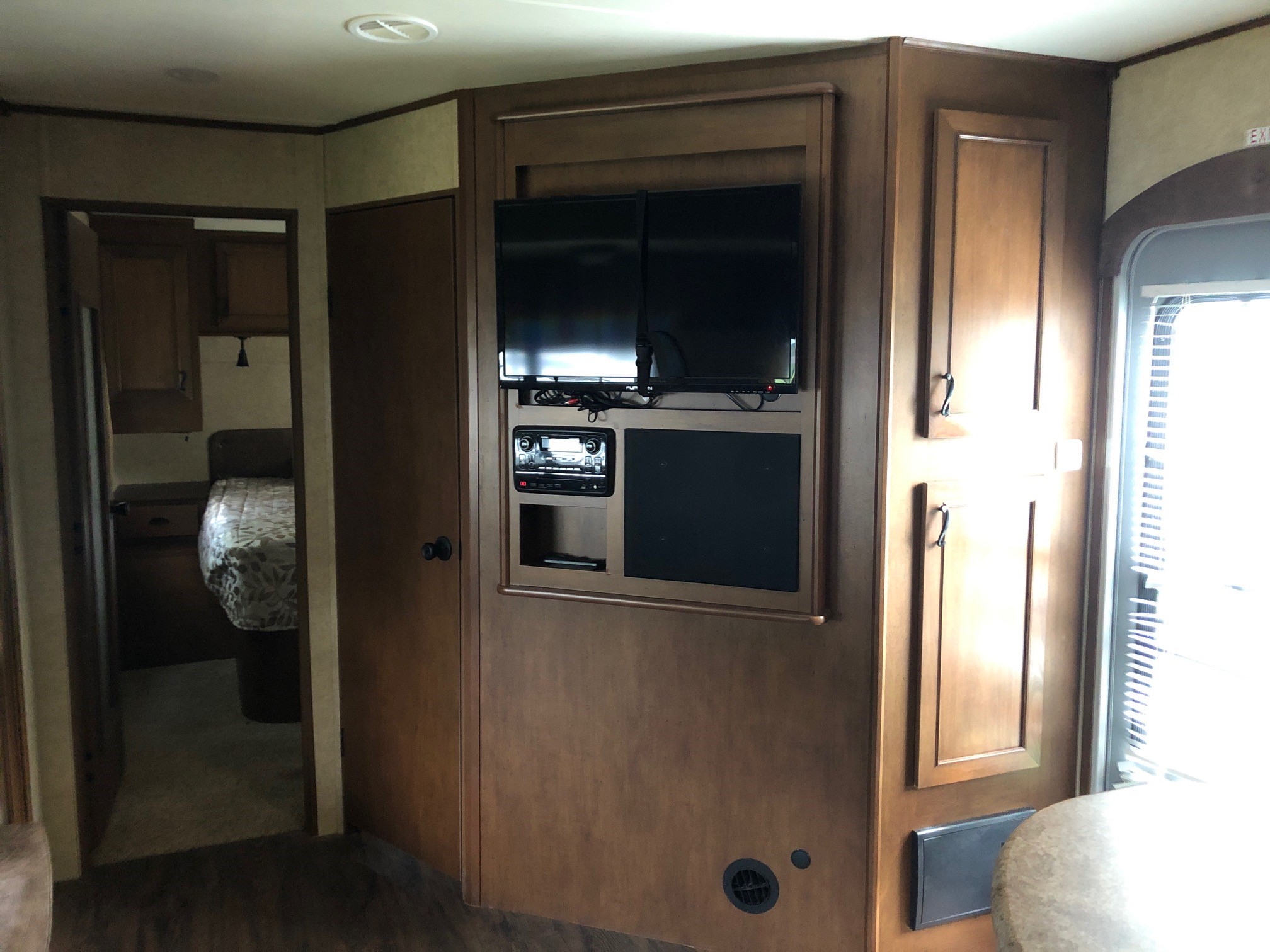 RV rental with a detailed wood-paneled interior, featuring a built-in entertainment center with dual TVs & a clear view into the bedroom.. Open Range Light 2015