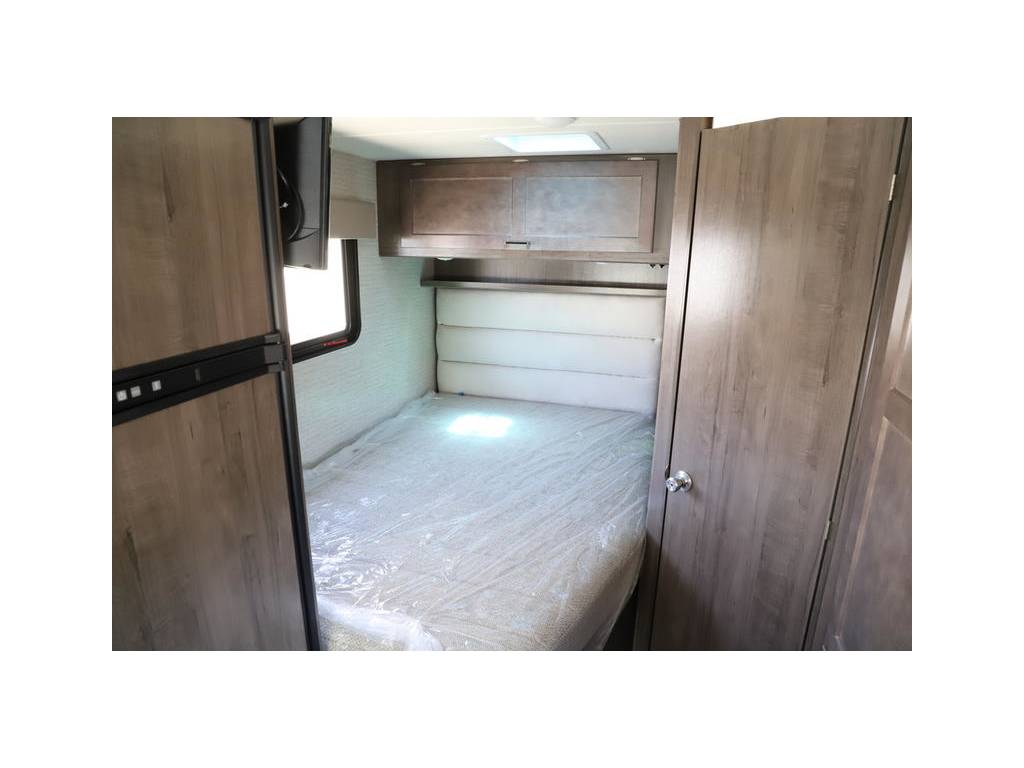 RV rental interior: bedroom with bed (plastic covered), window, fridge, overhead cabinet, and wardrobe.. Winnebago Minnie Winnie 2018