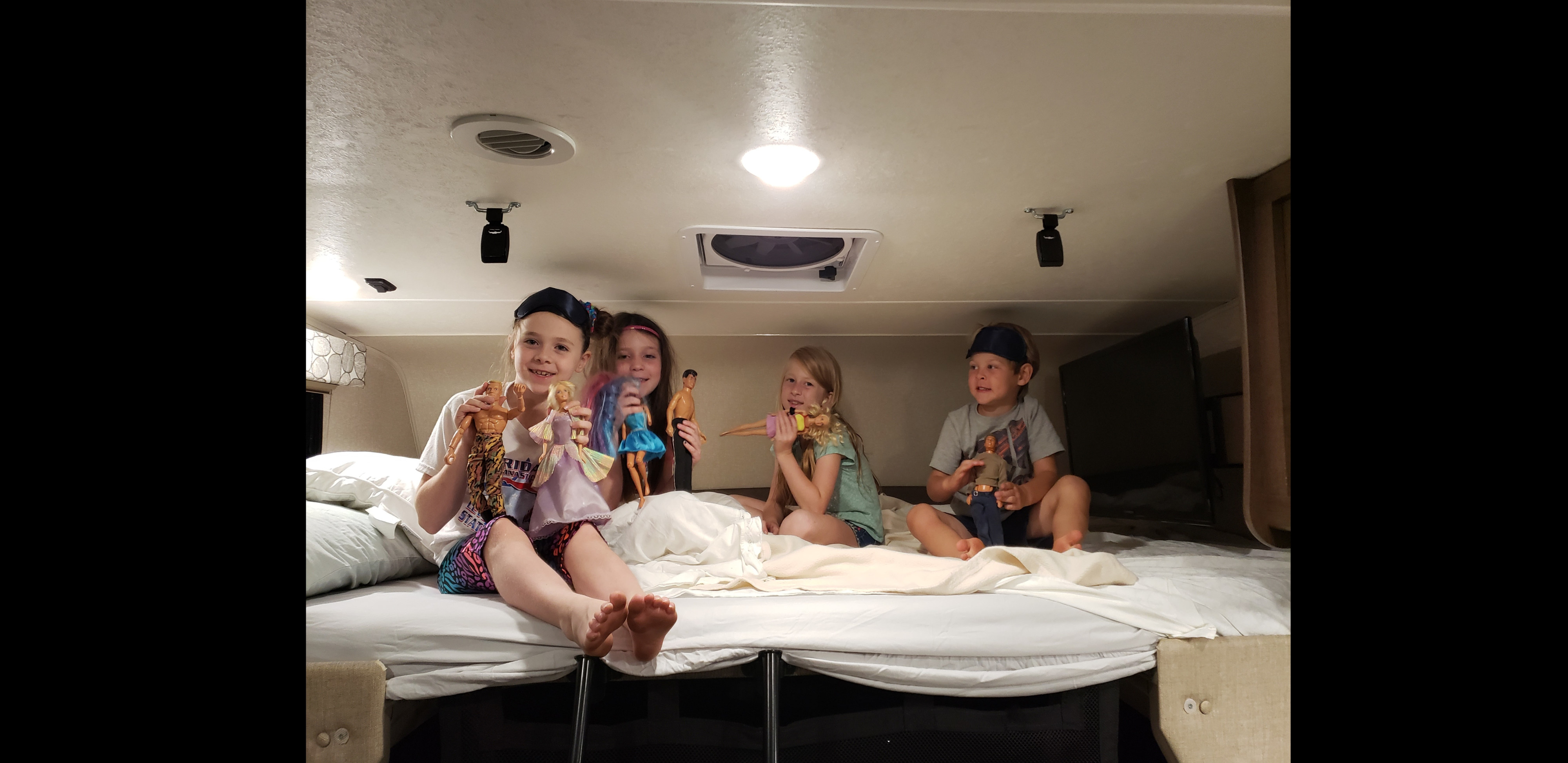 Four children play with dolls on a bed inside an RV rental, enjoying their travels. Happy family fun on the road.. Coachmen Freelander BH31 2019