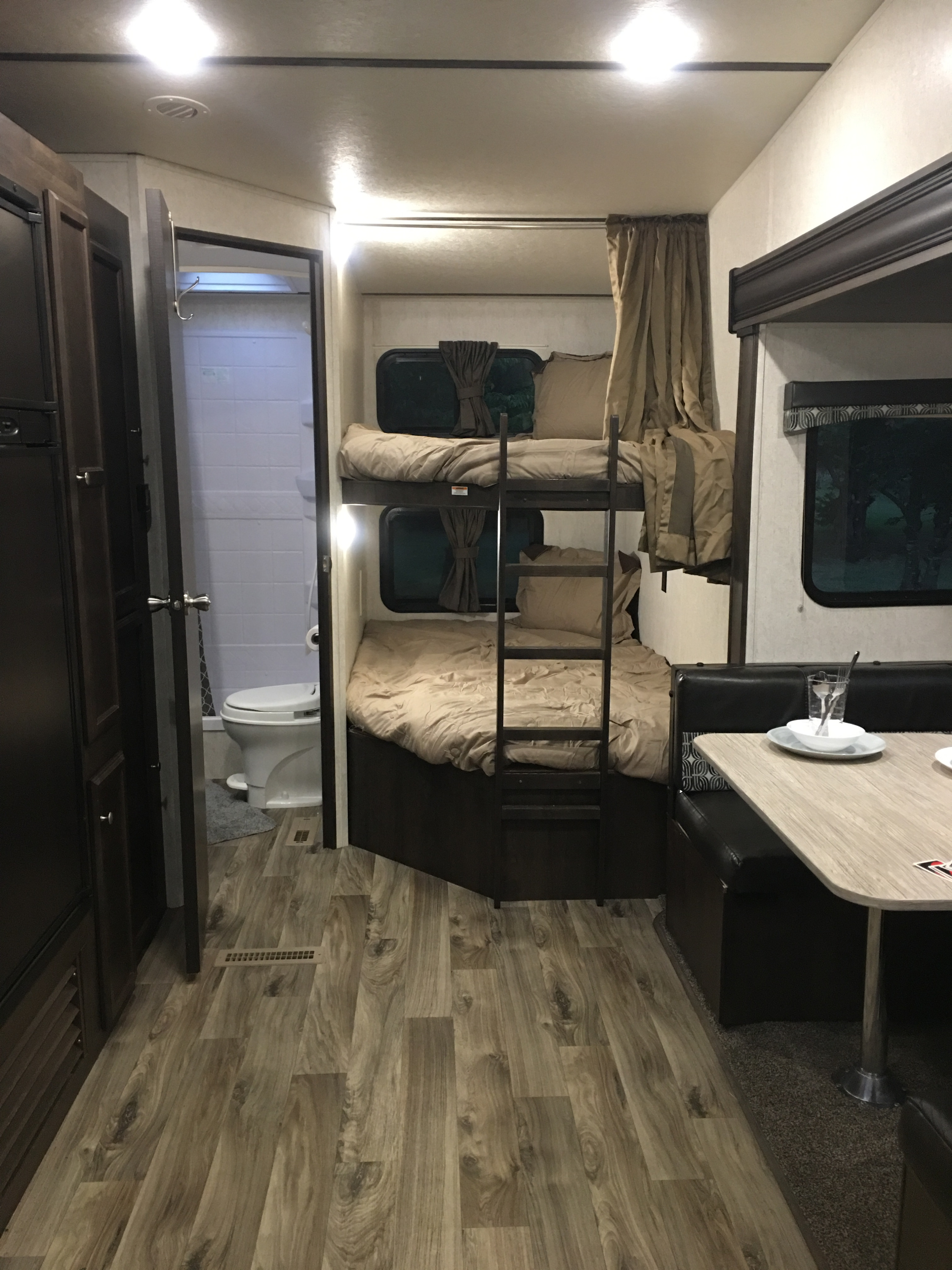 RV rental interior featuring bunk beds, a dinette, and bathroom access. Note the wood-look flooring and bright overhead lighting.. Starcraft Autumn Ridge 2018