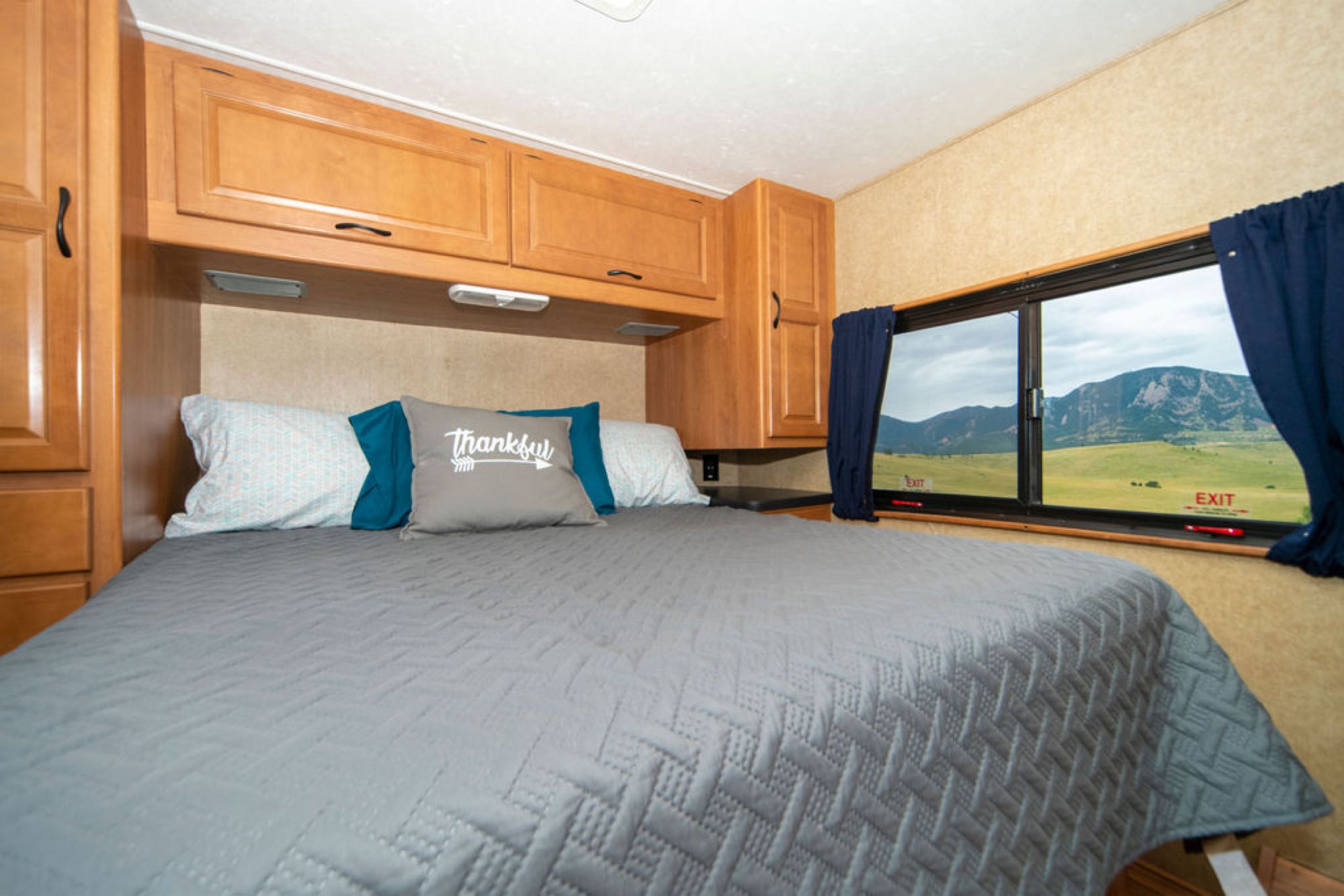 Cozy RV rental bedroom with a comfy bed, "Thankful" pillow, wooden cabinets, and scenic mountain views from the exit window.. Other Other 2015