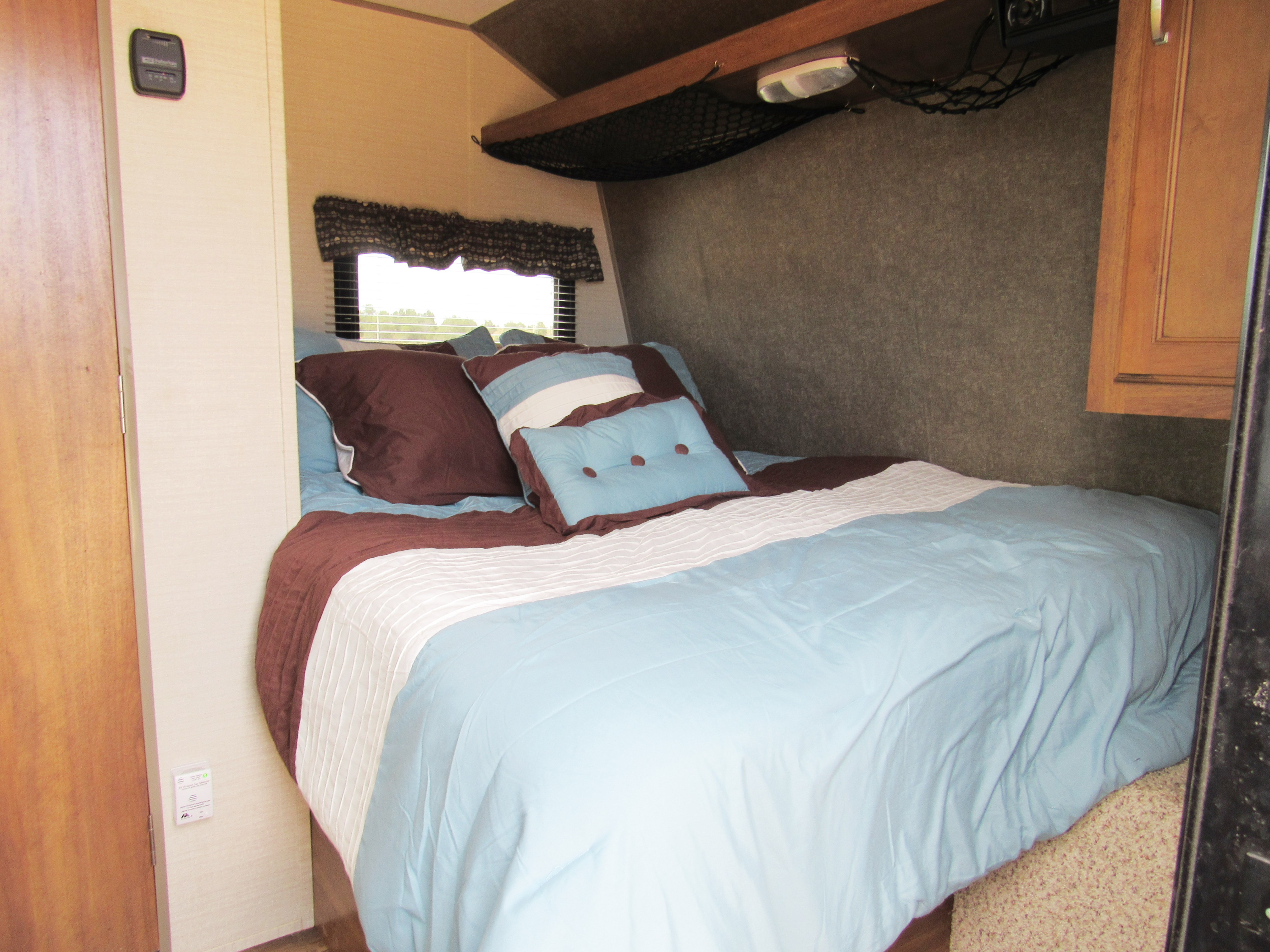 Comfortable RV rental bedroom with blue and brown bedding, compact storage, and a window for scenic views.. Other Other 2017