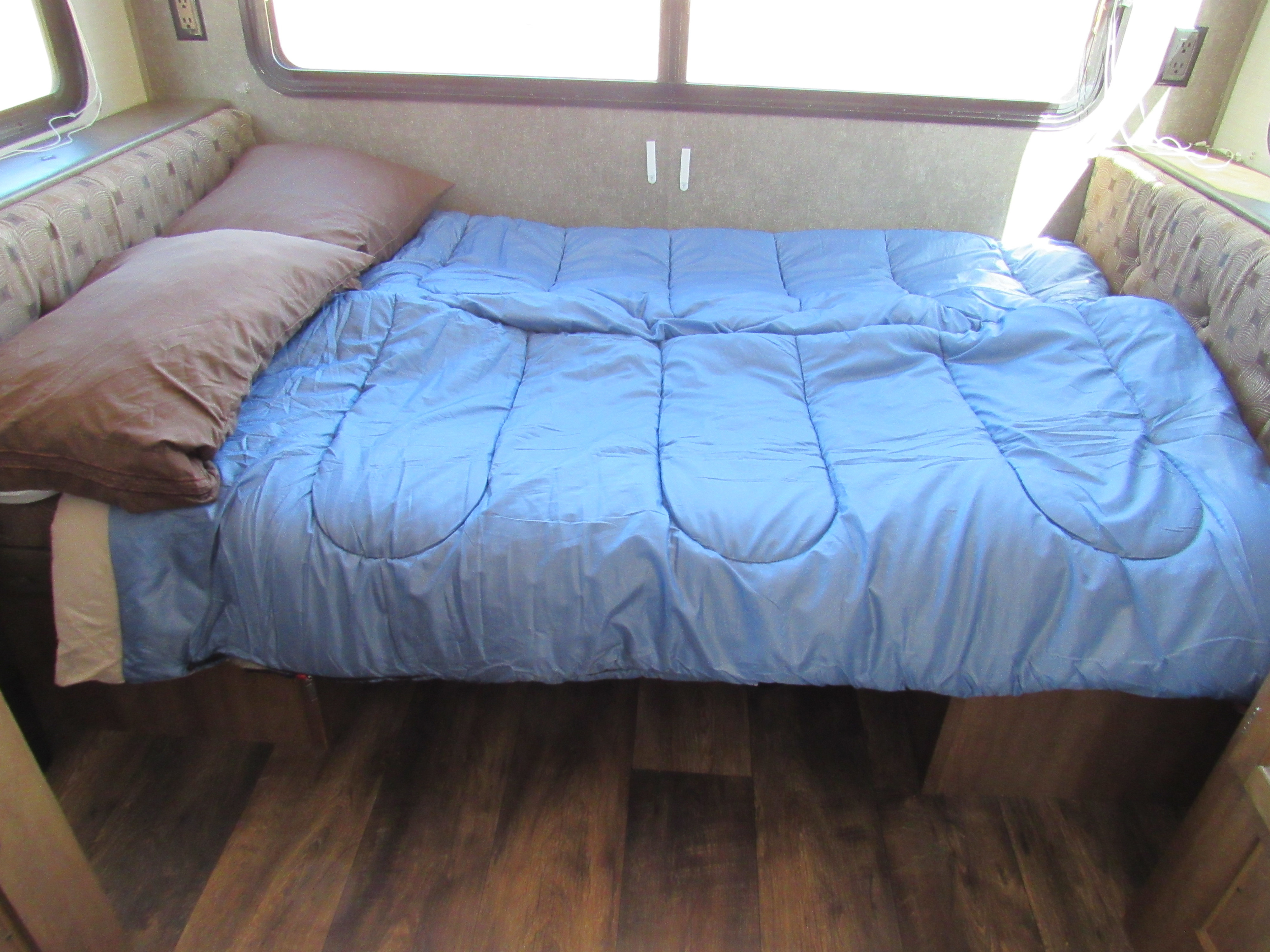 This RV rental offers a comfortable sleeping area with a blue comforter, brown pillows, and adjacent dinette benches.. Other Other 2017