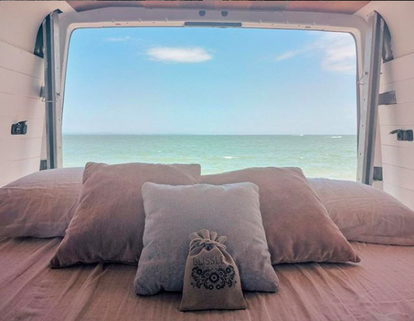 Cozy RV rental bed with pillows faces the ocean, offering tranquil views. Relax with your Blissle pouch.. Mercedes-Benz Sprinter 2005