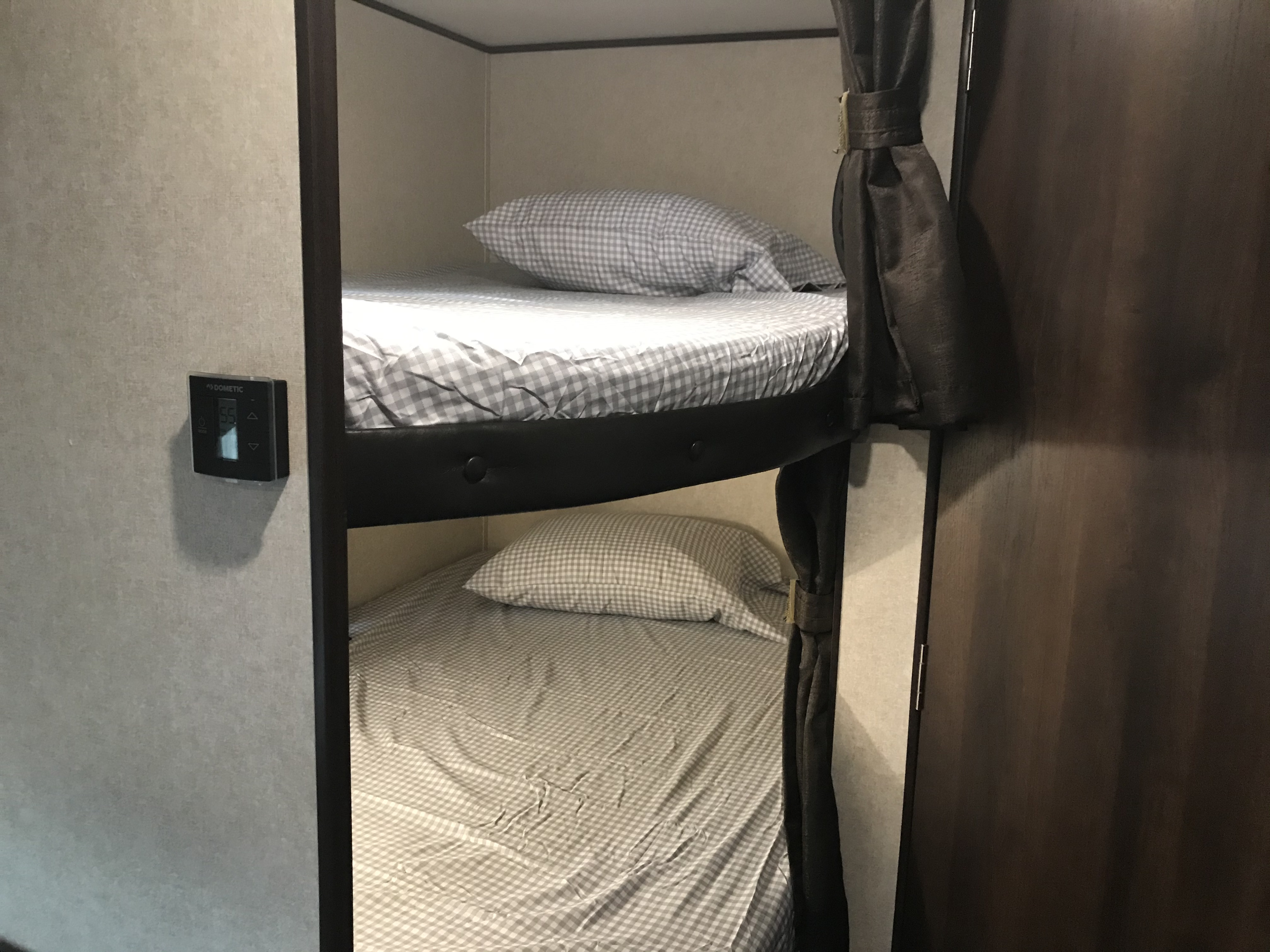 Cozy RV rental bunk beds, featuring gray checkered bedding, privacy curtain, and a Dometic control panel for comfort.. Jayco Jay Flight SLX 2019
