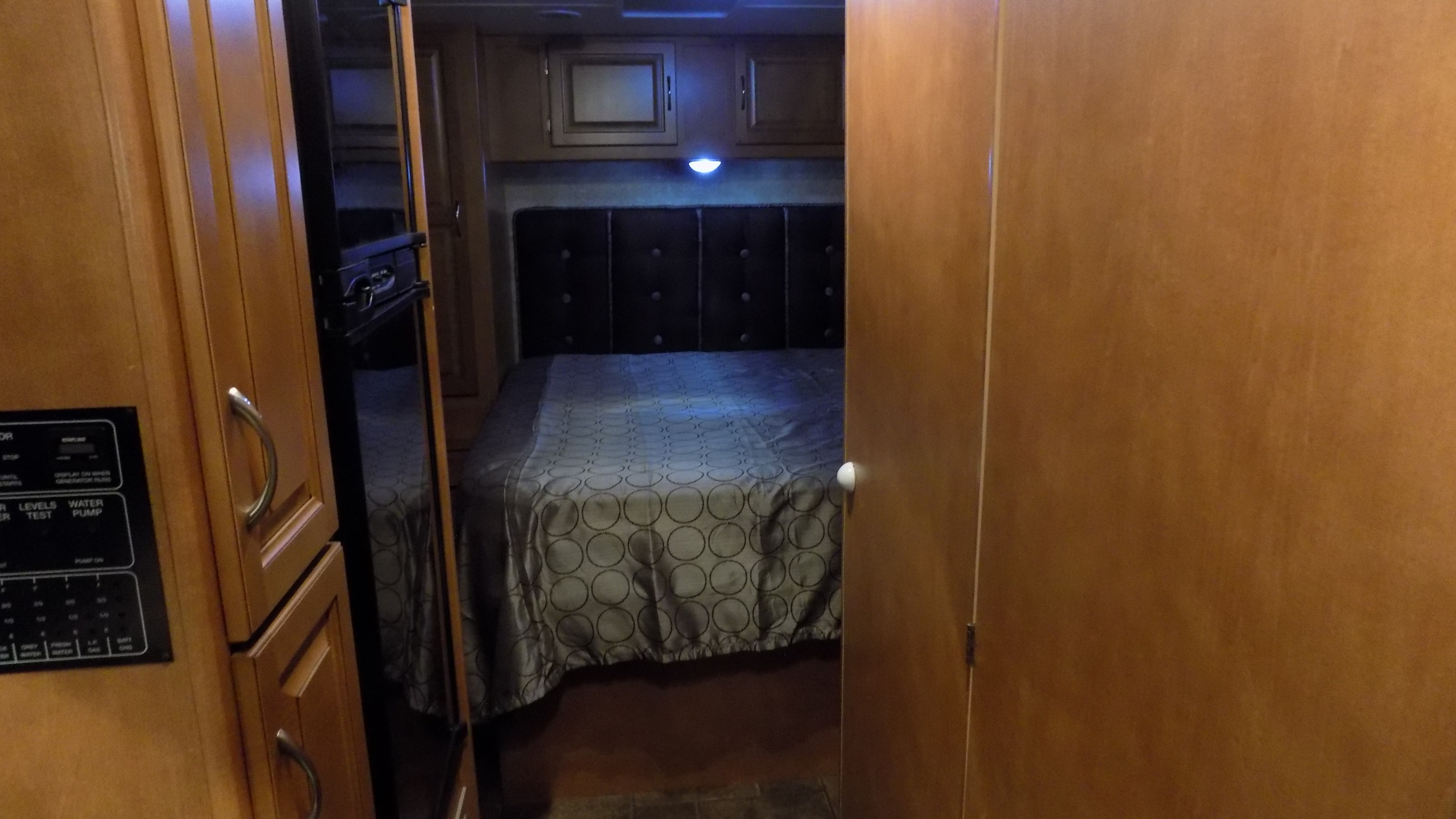 Cozy rv rental bedroom featuring a comfortable bed, overhead cabinets, and a side control panel for convenience.. Winnebago Minnie Winnie 2014