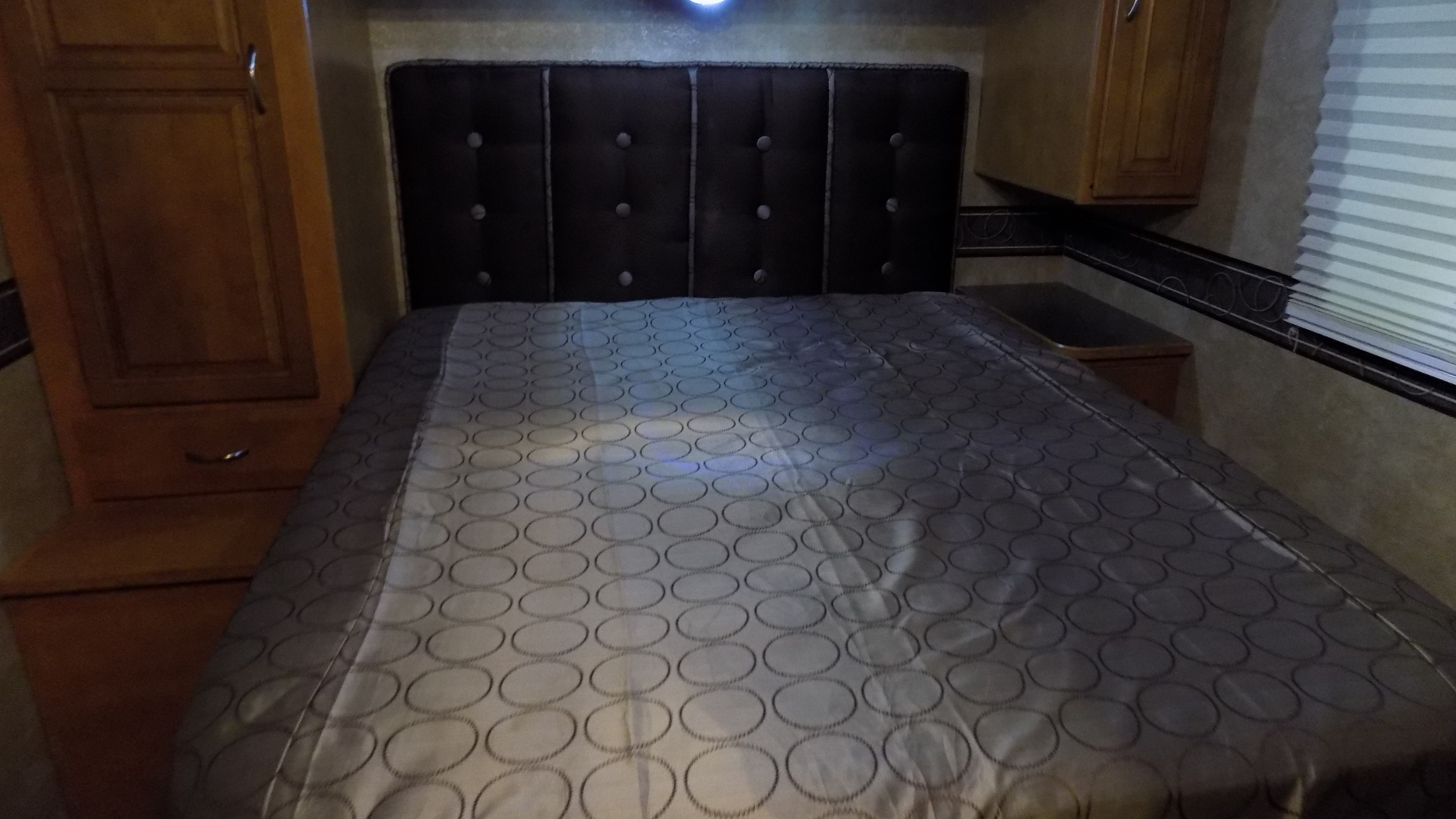 Comfortable RV rental bedroom featuring a bed with a dark, tufted headboard, and practical wooden storage on both sides.. Winnebago Minnie Winnie 2014